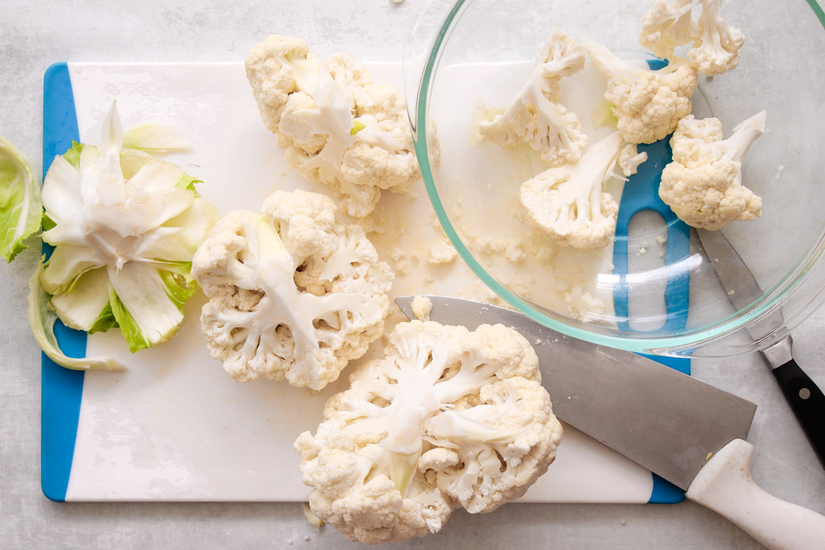 overhead image of prepping a large cauliflower floret on a cutting board. 