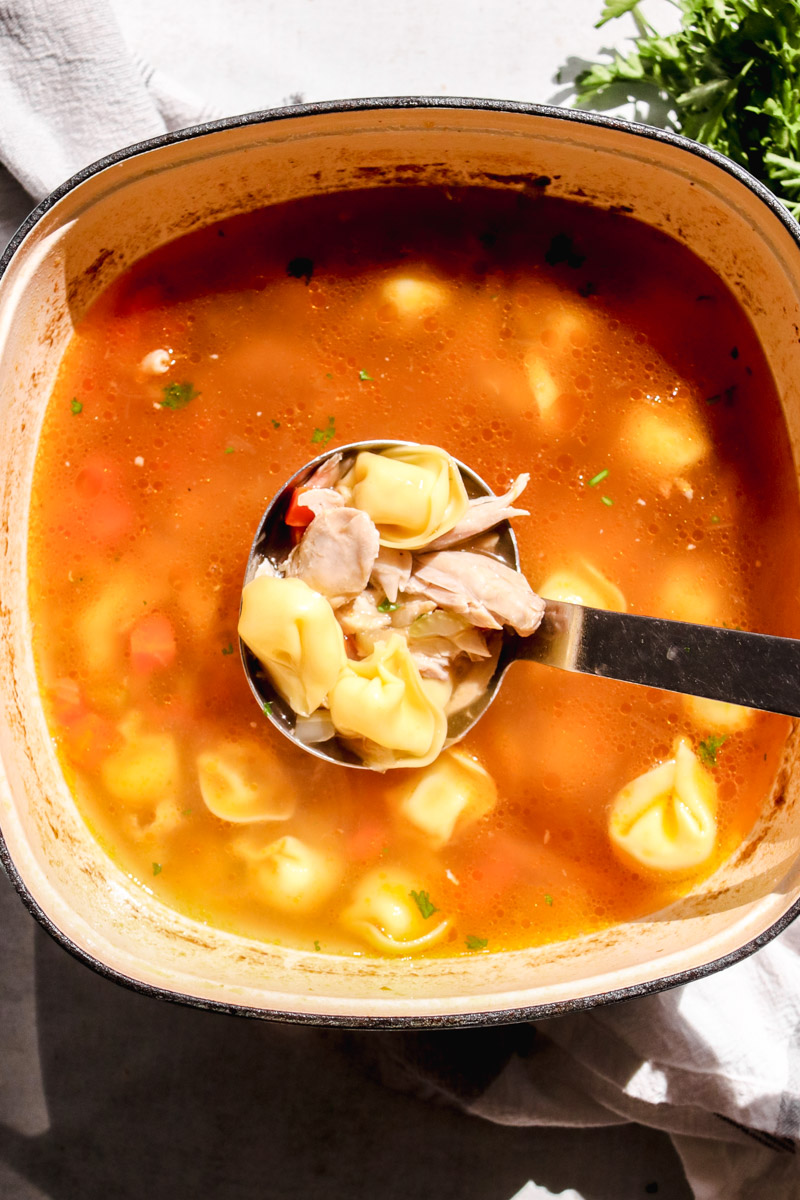 overhead image of a ladle lifting chicken tortellini soup. 