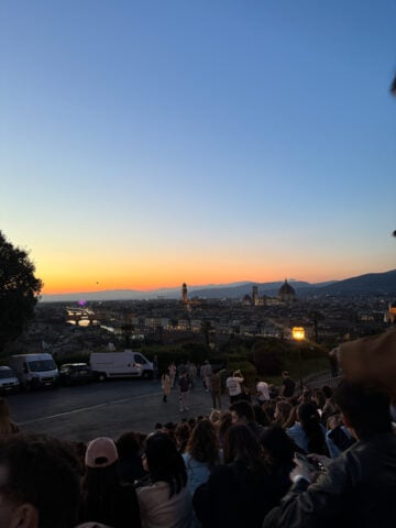 A crowd of people sits on steps overlooking Florence at sunset, enjoying the cityscape-including the Duomo and Palazzo Vecchio-against a colorful sky of blue and orange hues, capturing the essence of exploring Florence in One Day.