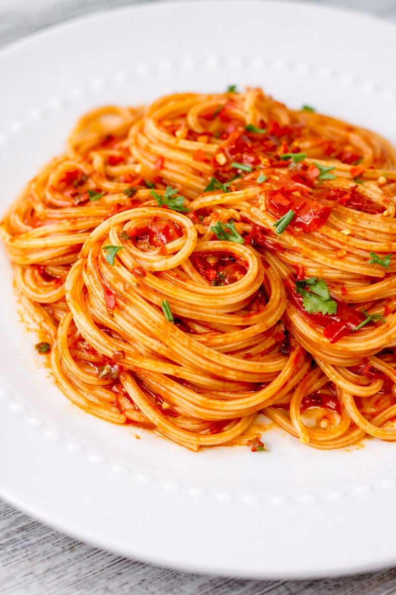 A close-up of a plate of Caramelized Shallot Pasta topped with tomato sauce and garnished with chopped herbs, served on a white dish.