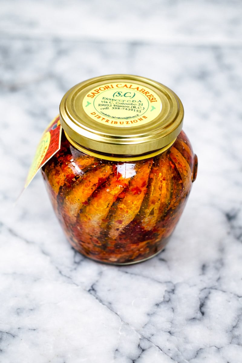 A glass jar of Italian eggplants preserved in oil, seasoned with red spices—perfect for pairing with Caramelized Shallot Pasta—sits sealed with a gold “Sapori Calabresi” lid on a white marble surface.