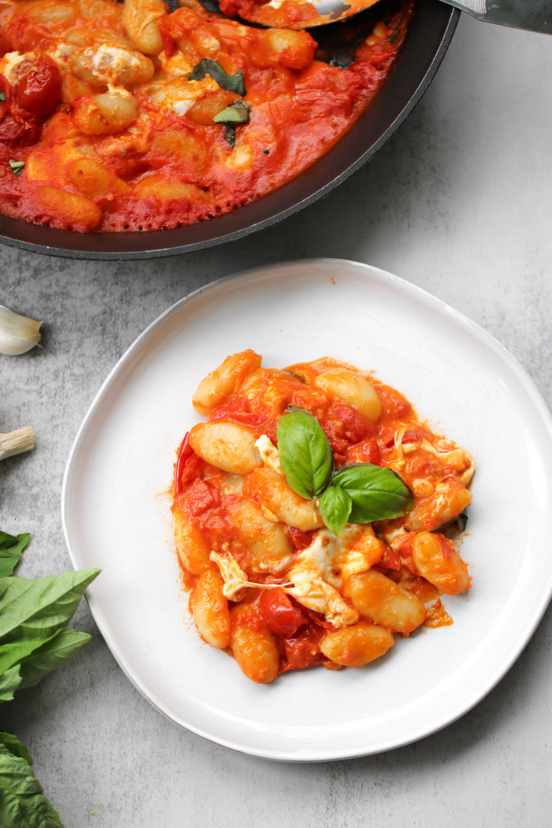 overhead image of gnocchi with tomato sauce cheese and basil on a white plate. 