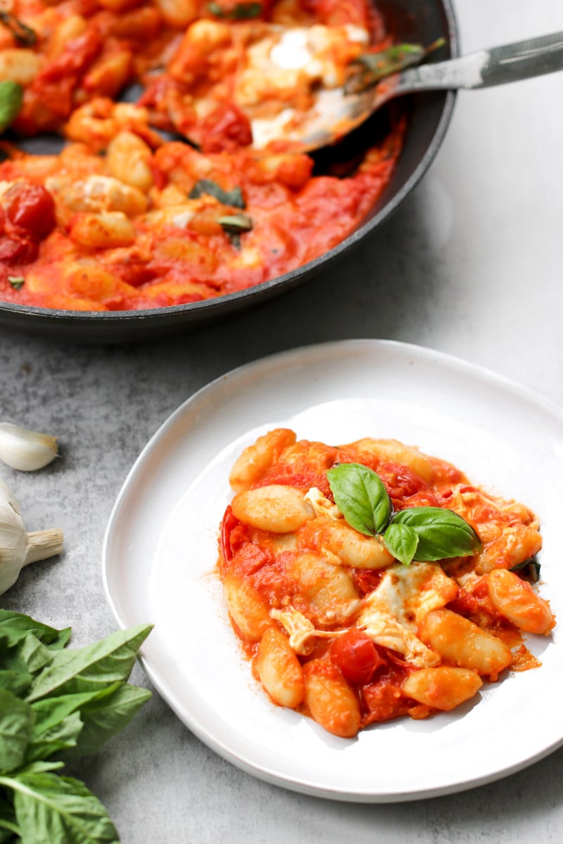 overhead image of gnocchi alla sorrentina in a skillet with basil in background.