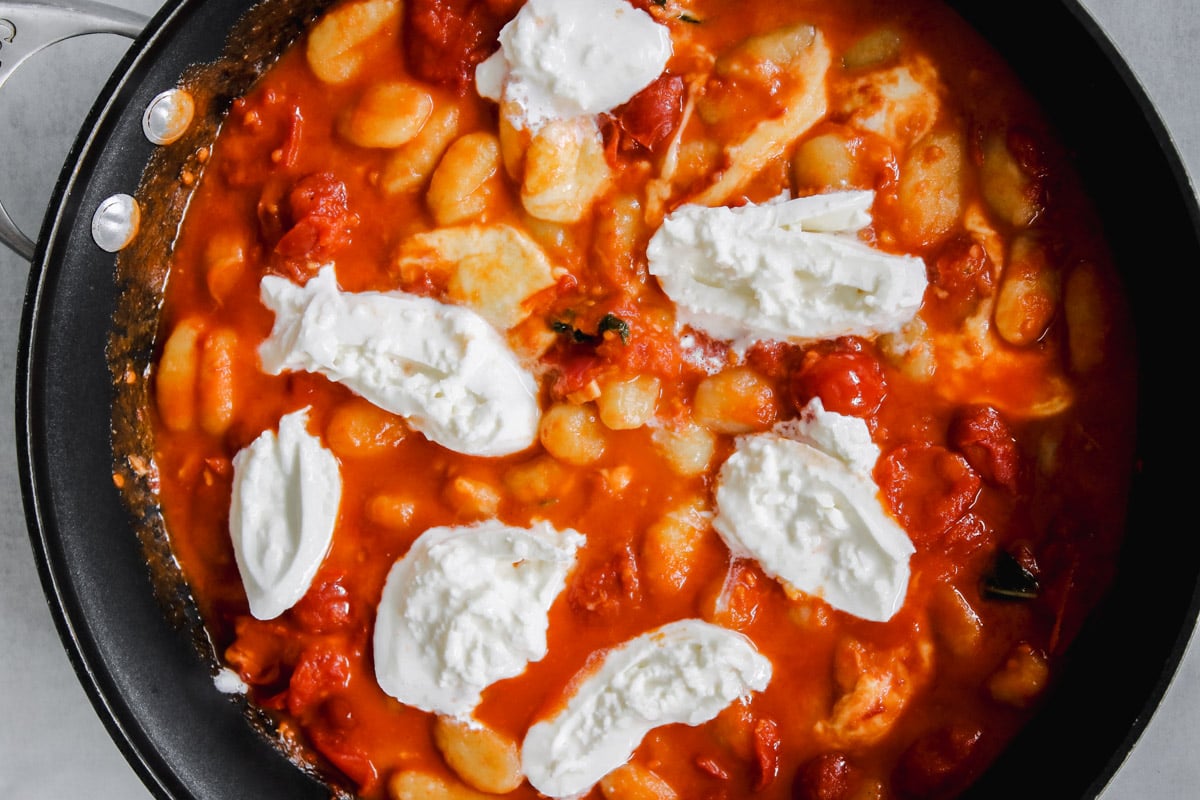 overhead image of mozzarella cheese on gnocchi in a skillet.