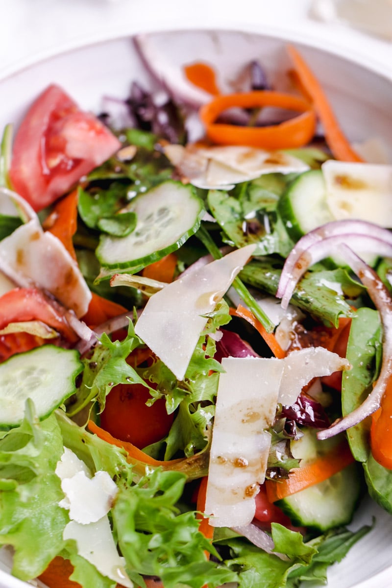 close up image of a mixed green salad in a white bowl.