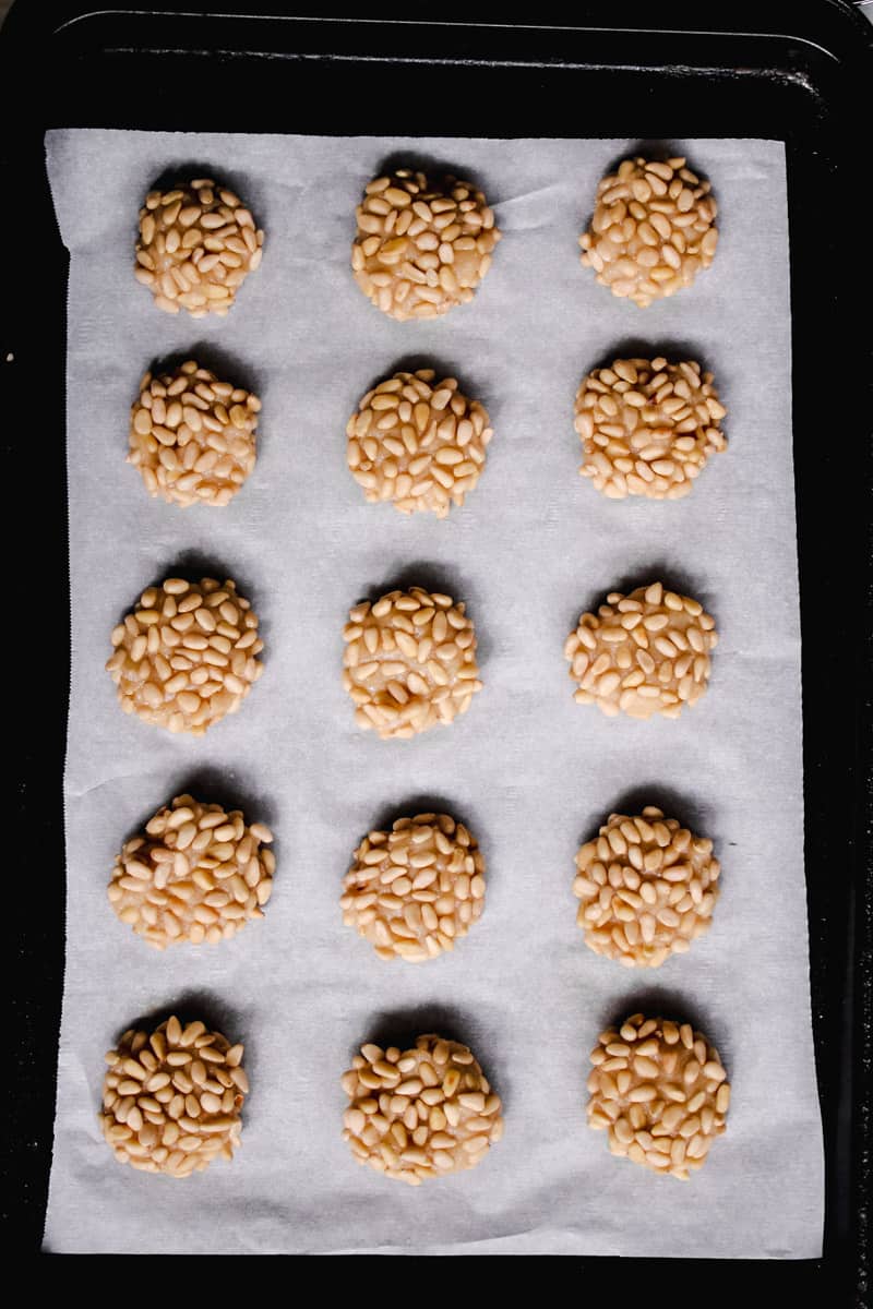 overhead image of pignoli cookies on a parchment lined baking sheet.