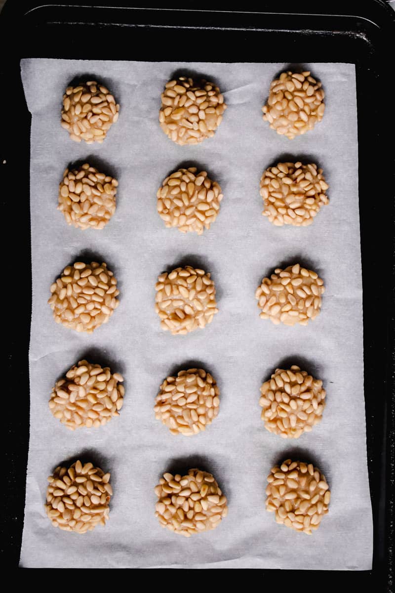 overhead image of pignoli cookies on a parchment lined baking sheet. 