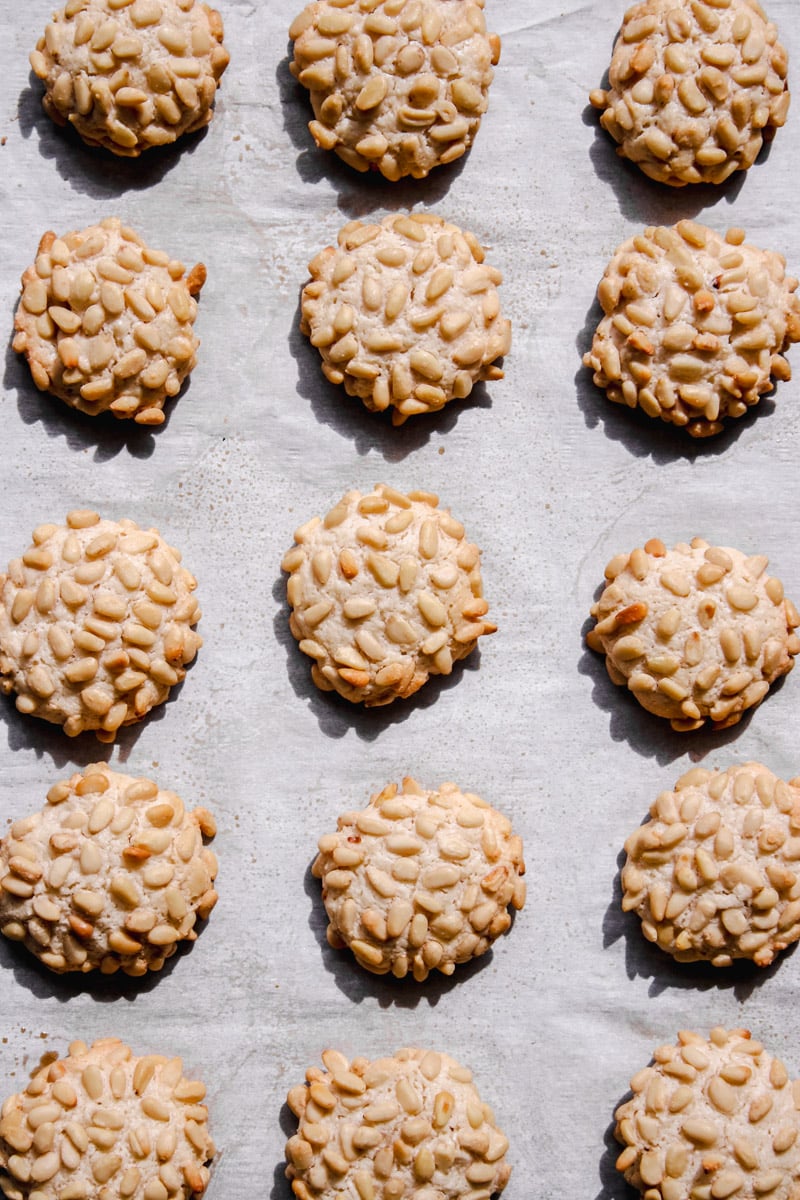 overhead image of pignoli cookies on a paper lined tray.