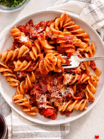 A bowl of fusilli amatriciana in a tomato-based sauce with bits of meat and a dusting of grated cheese, served with a fork.