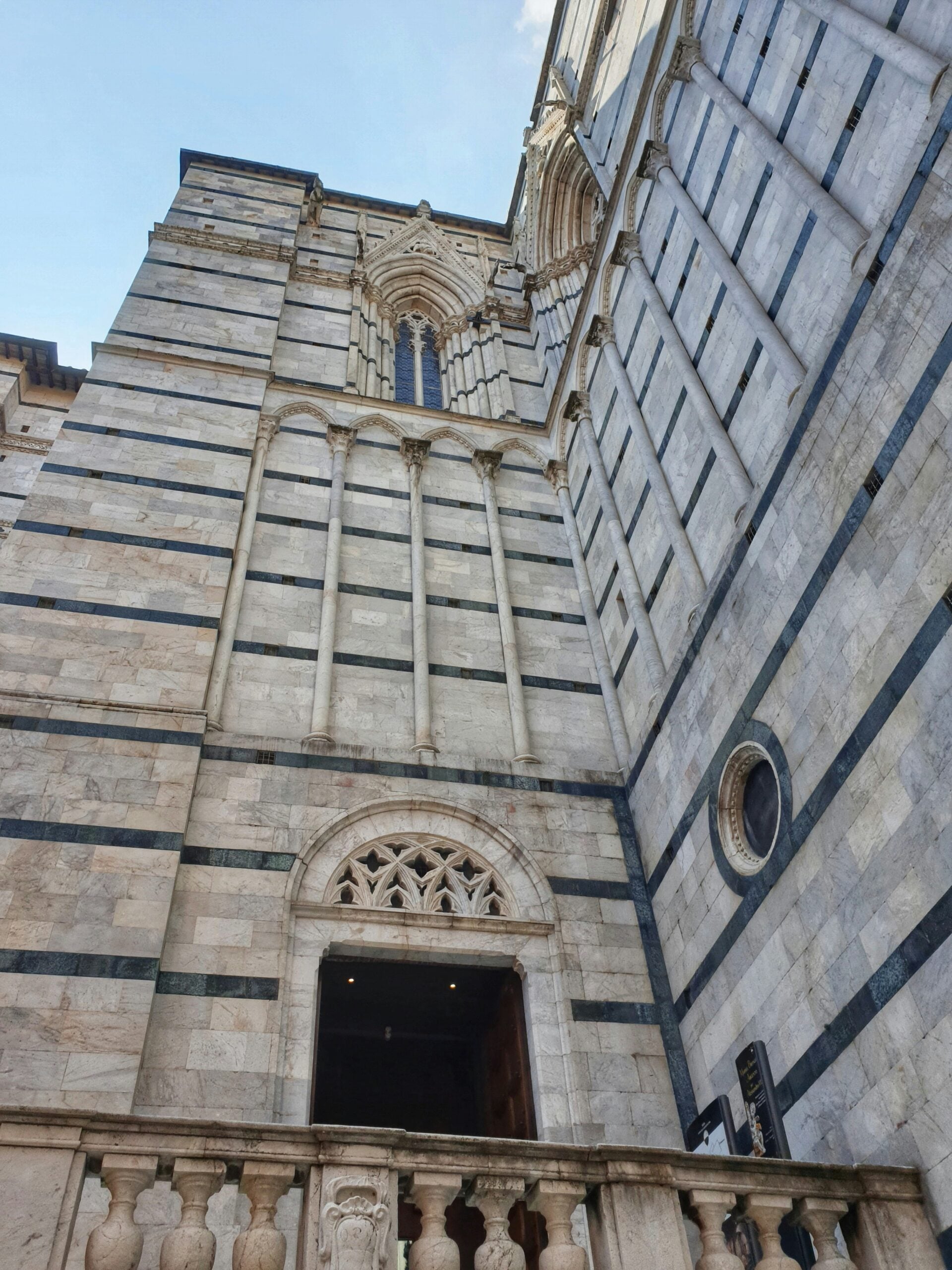 A detailed photograph of the facade of the old Siena Cathedral in Italy. The image showcases the intricate Gothic architecture, with its ornate marble inlays, sculptures, and decorative elements. The grand entrance, flanked by statues of saints and topped with a rose window, exemplifies the cathedral's historical and artistic significance. This stunning facade is a testament to Siena, Italy's rich cultural and religious heritage, attracting visitors from around the world.