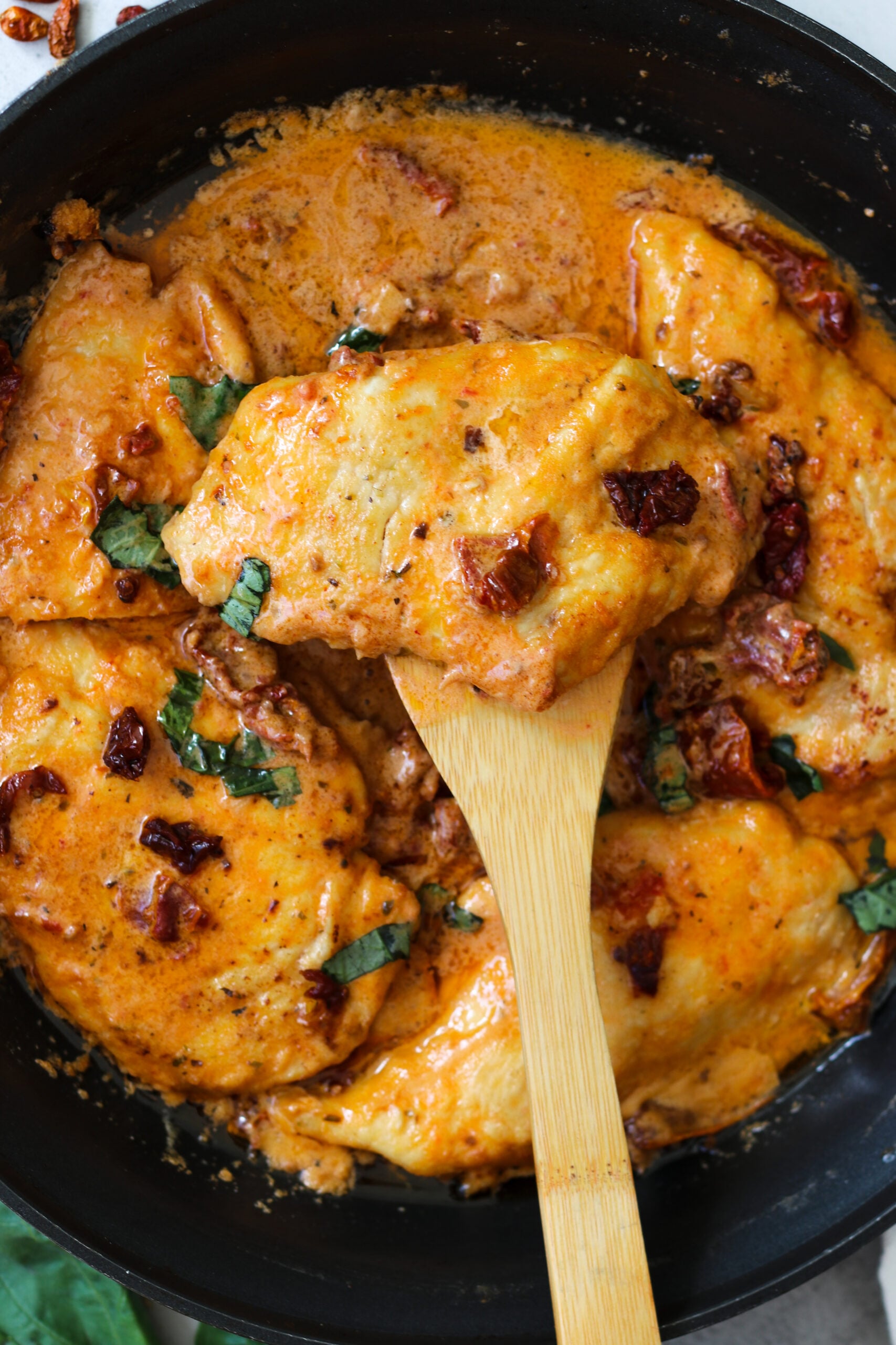 closeup image of chicken on a wooden spoon in a skillet.