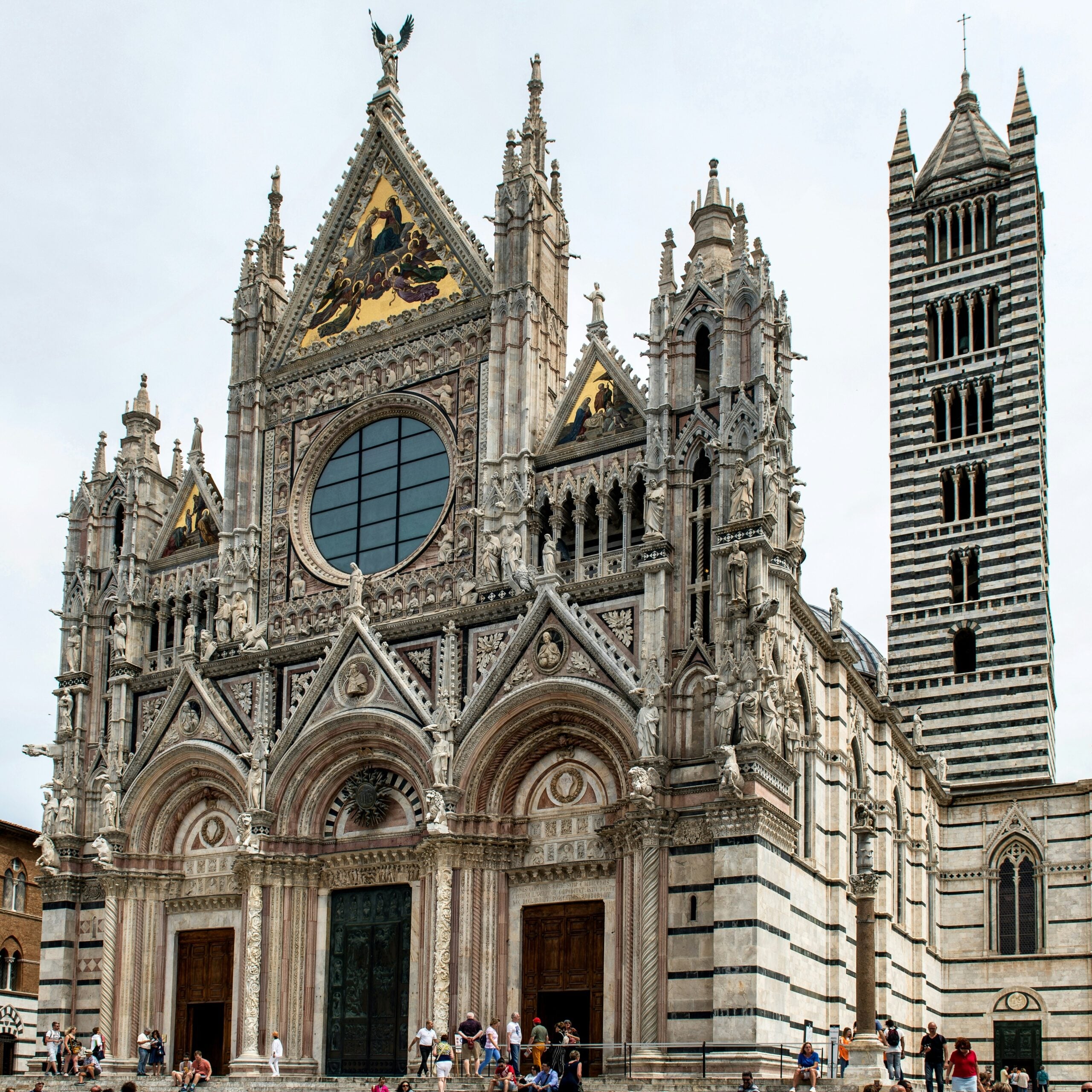 A magnificent view of the Siena Cathedral in Italy, capturing its awe-inspiring Gothic architecture. The photograph highlights the stunning facade adorned with intricate marble inlays, statues, and decorative elements. The grand rose window and towering spires reach towards the sky, emphasizing the cathedral's majestic presence. This image showcases the artistic and historical significance of the Siena Cathedral, a masterpiece that stands as a testament to the rich cultural heritage of Siena, Italy.