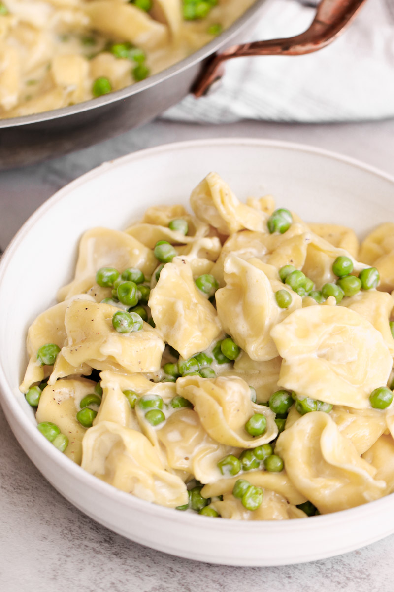 close up image of tortellini alla panna with peas in a white bowl. 