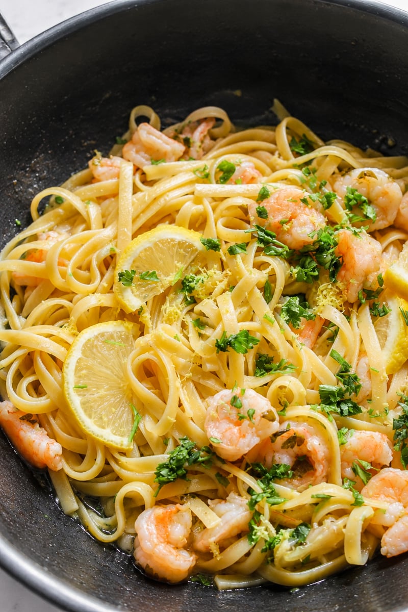 Easy Shrimp Scampi with Linguine: Fettuccine pasta with shrimp, lemon slices, and chopped parsley in a skillet, garnished with lemon zest and fresh herbs.