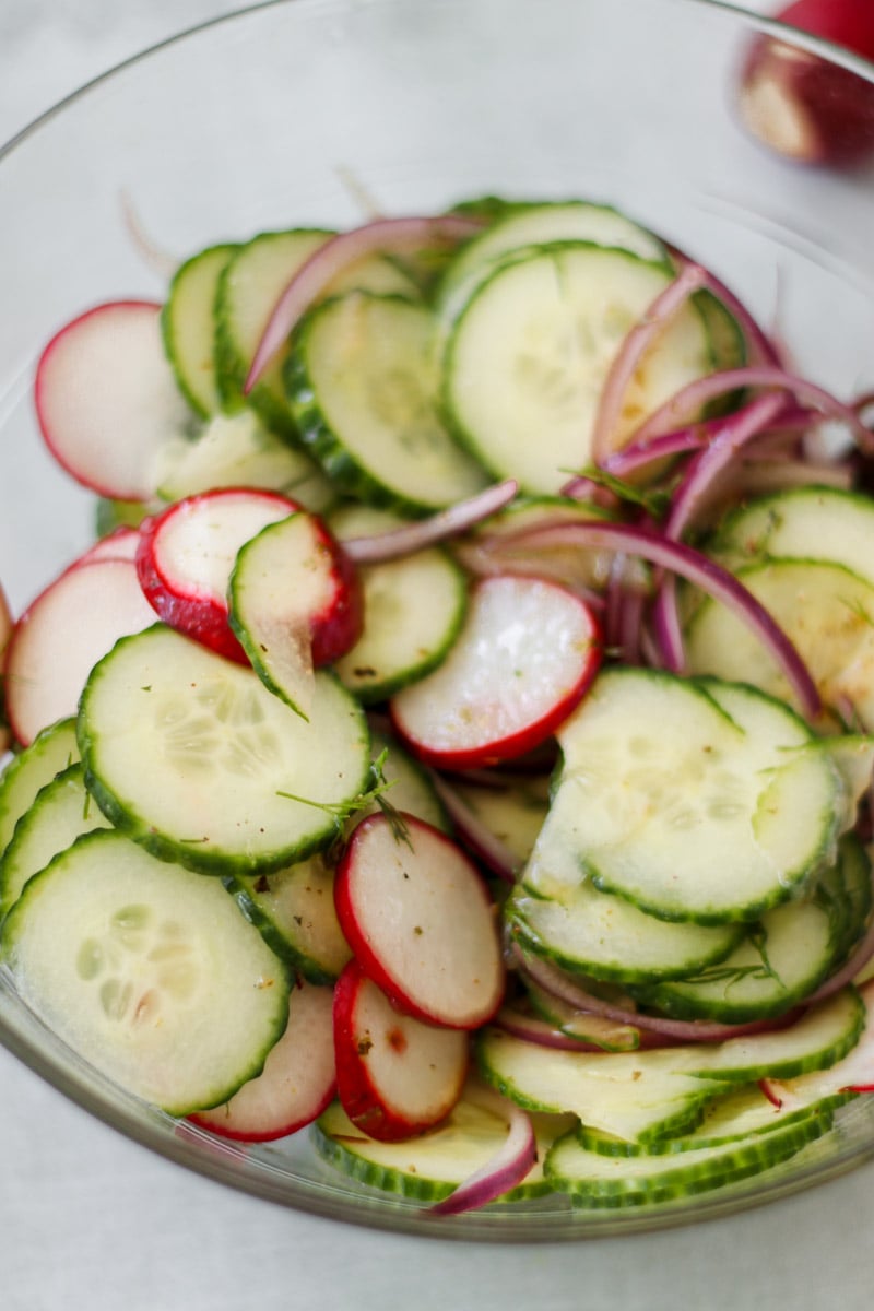 close-up image of cucumbers radishes red onions in a glass bowl.