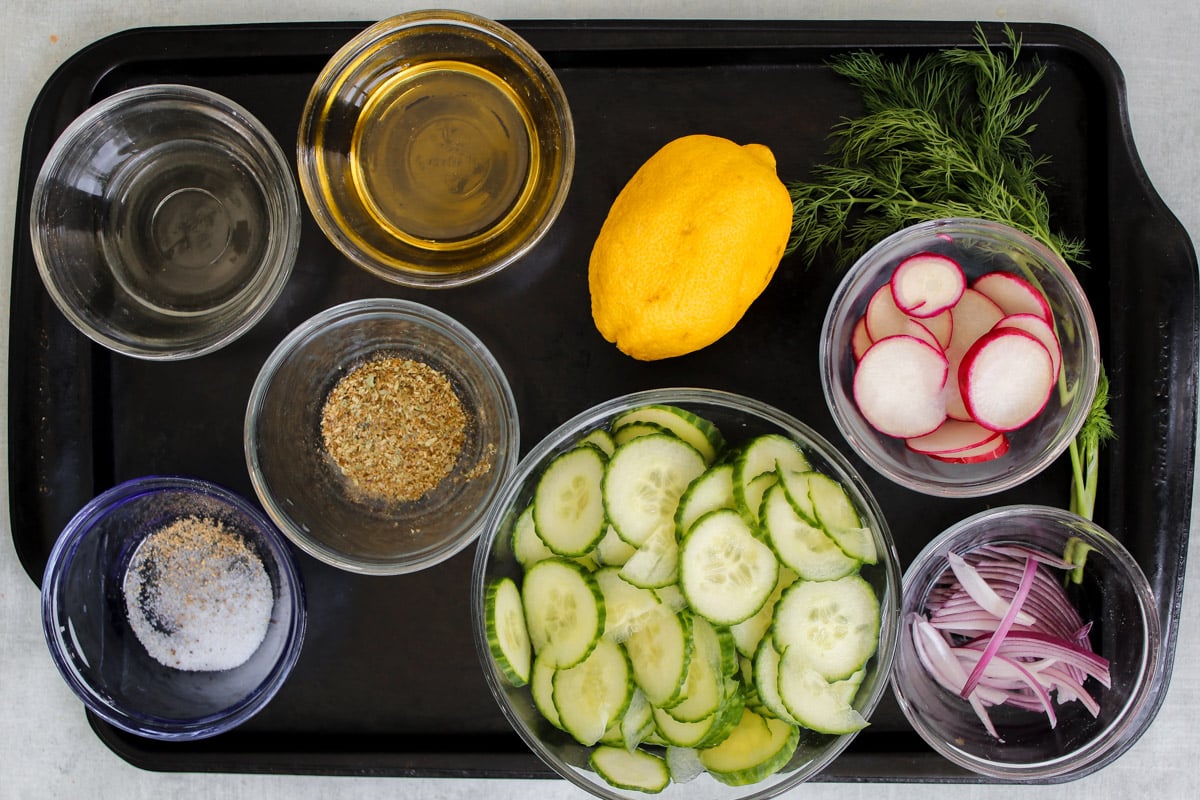 overhead image of ingredients to make cucumber salad on a baking sheet.