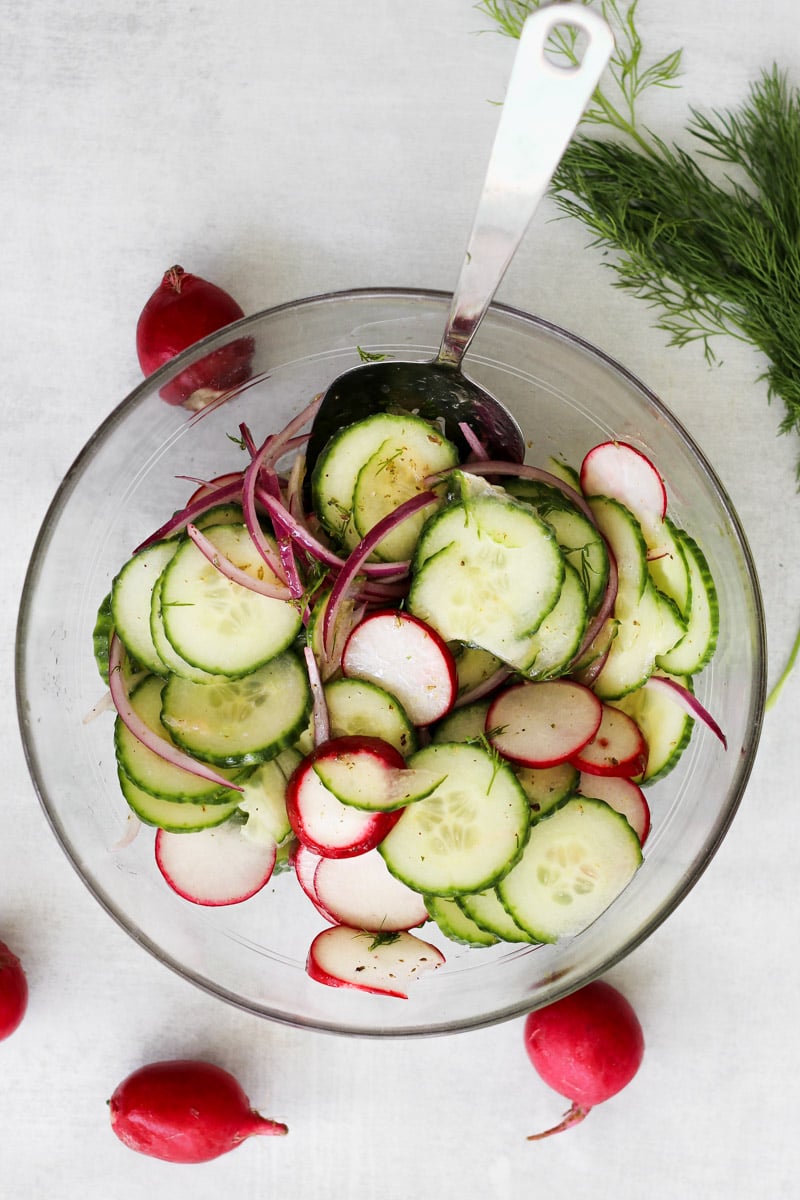 overhead image of cucumber salad in a glass bowl with a serving spoon.