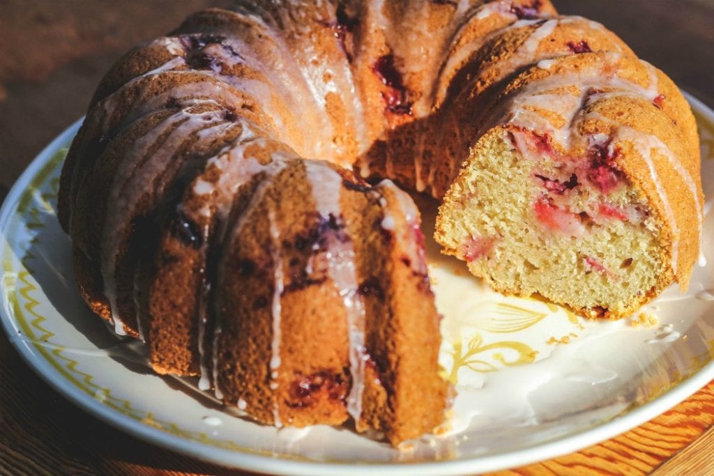 fresh strawberry bundt cake with slice cut out on a white plate.