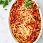 Baked Pasta with Tomatoes and Eggplant in a white oval dish topped with melted cheese, tomato sauce, and fresh basil, with basil sprigs on the side.