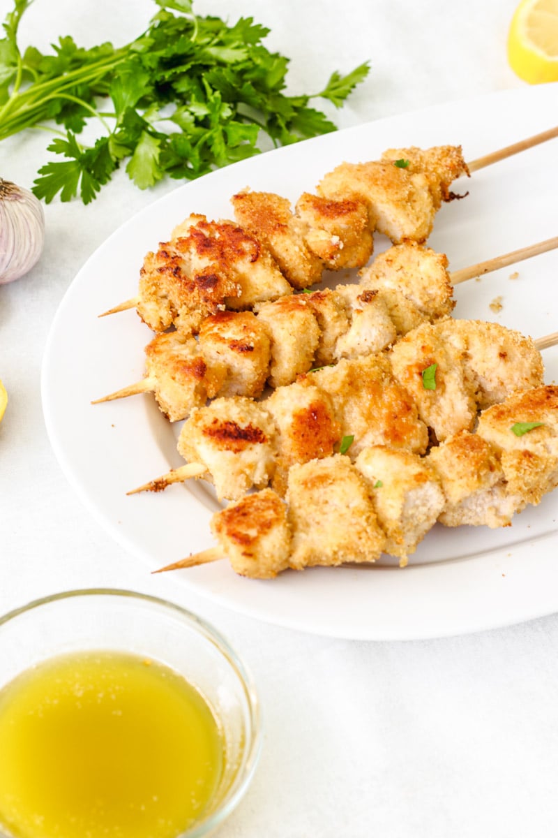 close up image of chicken spiedini with parsley in background and a lemon butter sauce in a bowl.