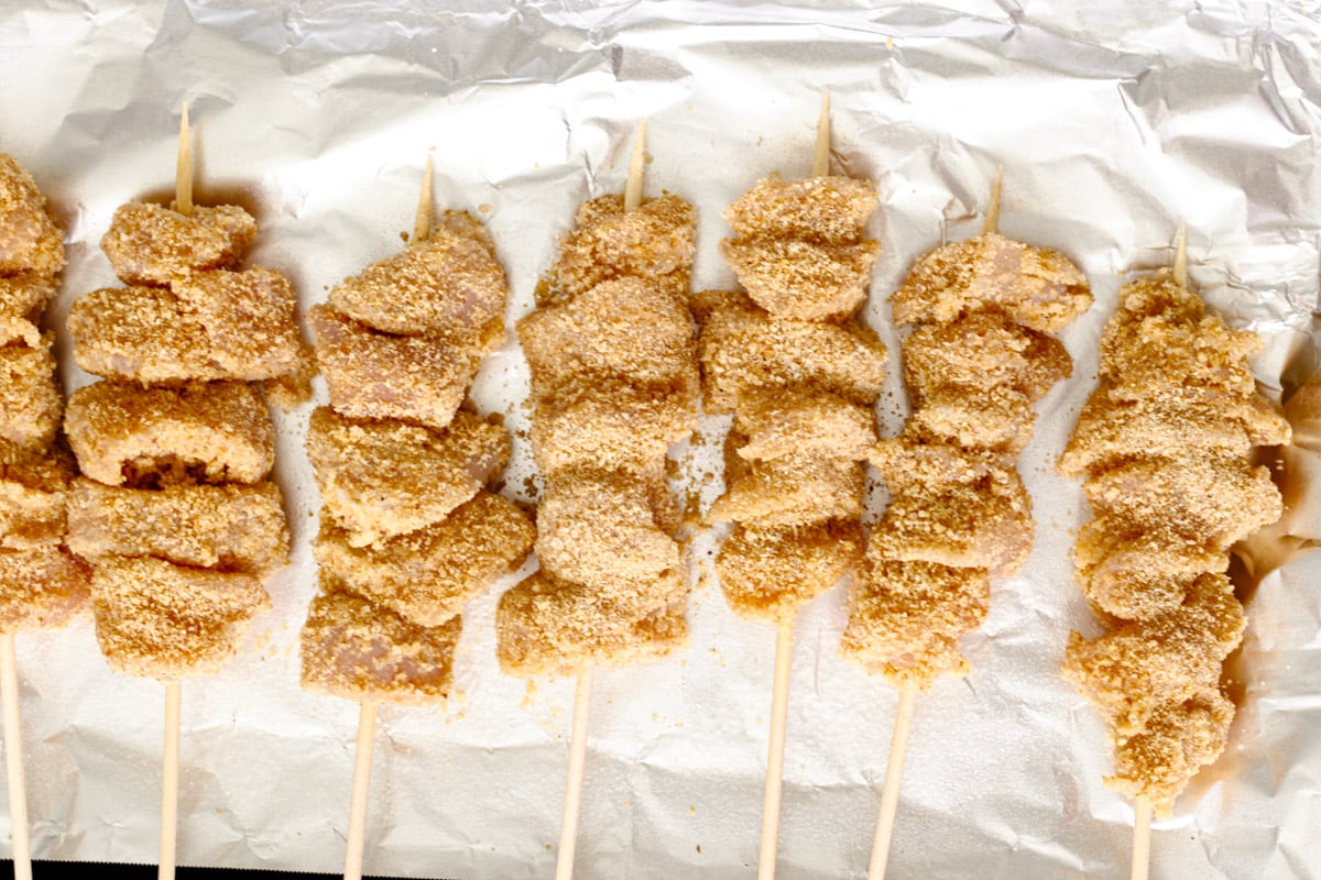 overhead image of chicken skewers on a foil lined baking sheet.
