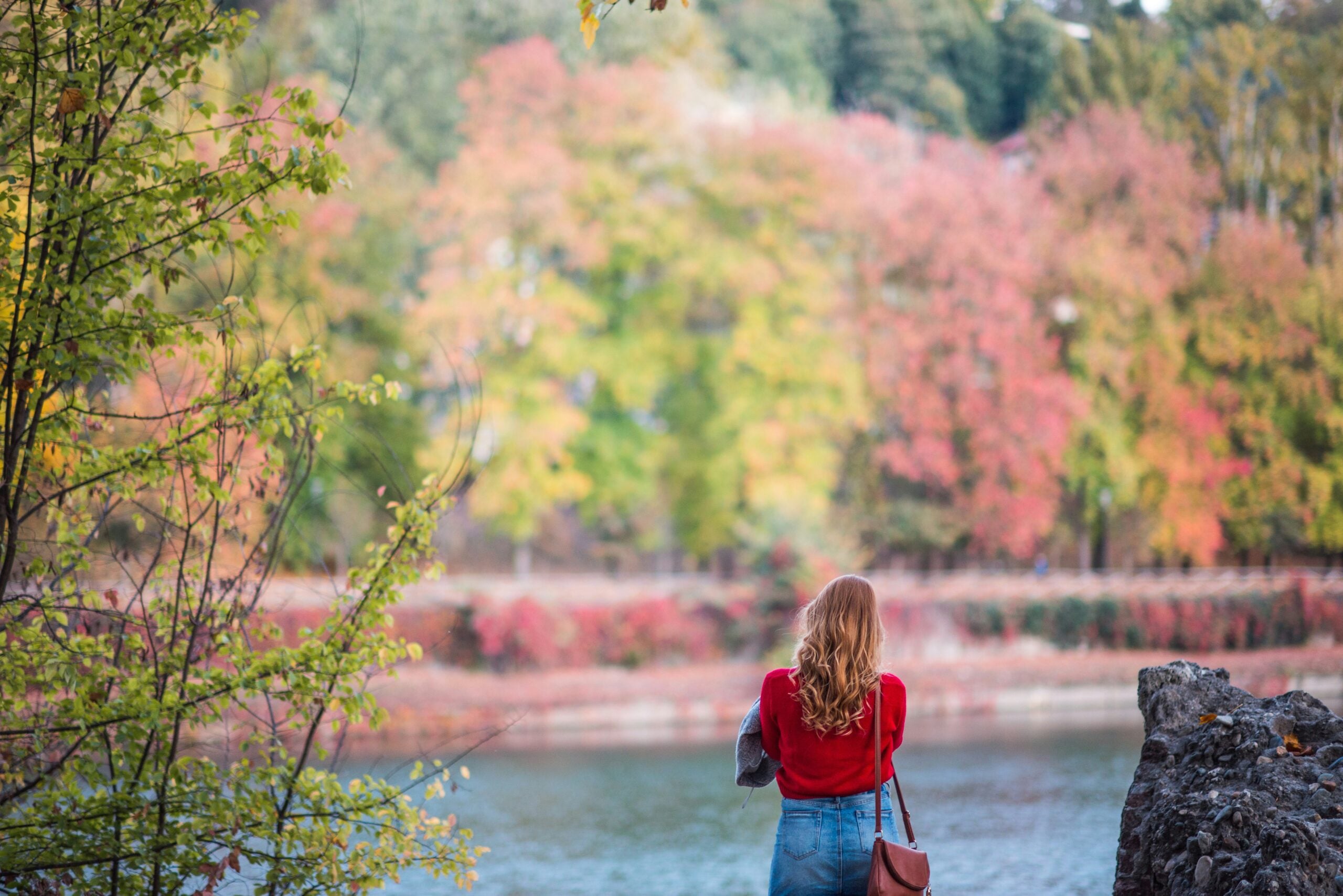 A blonde girl gazes thoughtfully at the River Po in Turin during the fall, surrounded by the vibrant hues of colorful trees. The golden, orange, and red foliage creates a picturesque backdrop, enhancing the serene atmosphere of the scene. Is Turin worth visiting? Absolutely! This beautiful moment captures the enchanting autumnal charm of Turin, making it an ideal destination for nature lovers and those seeking tranquil, scenic views.