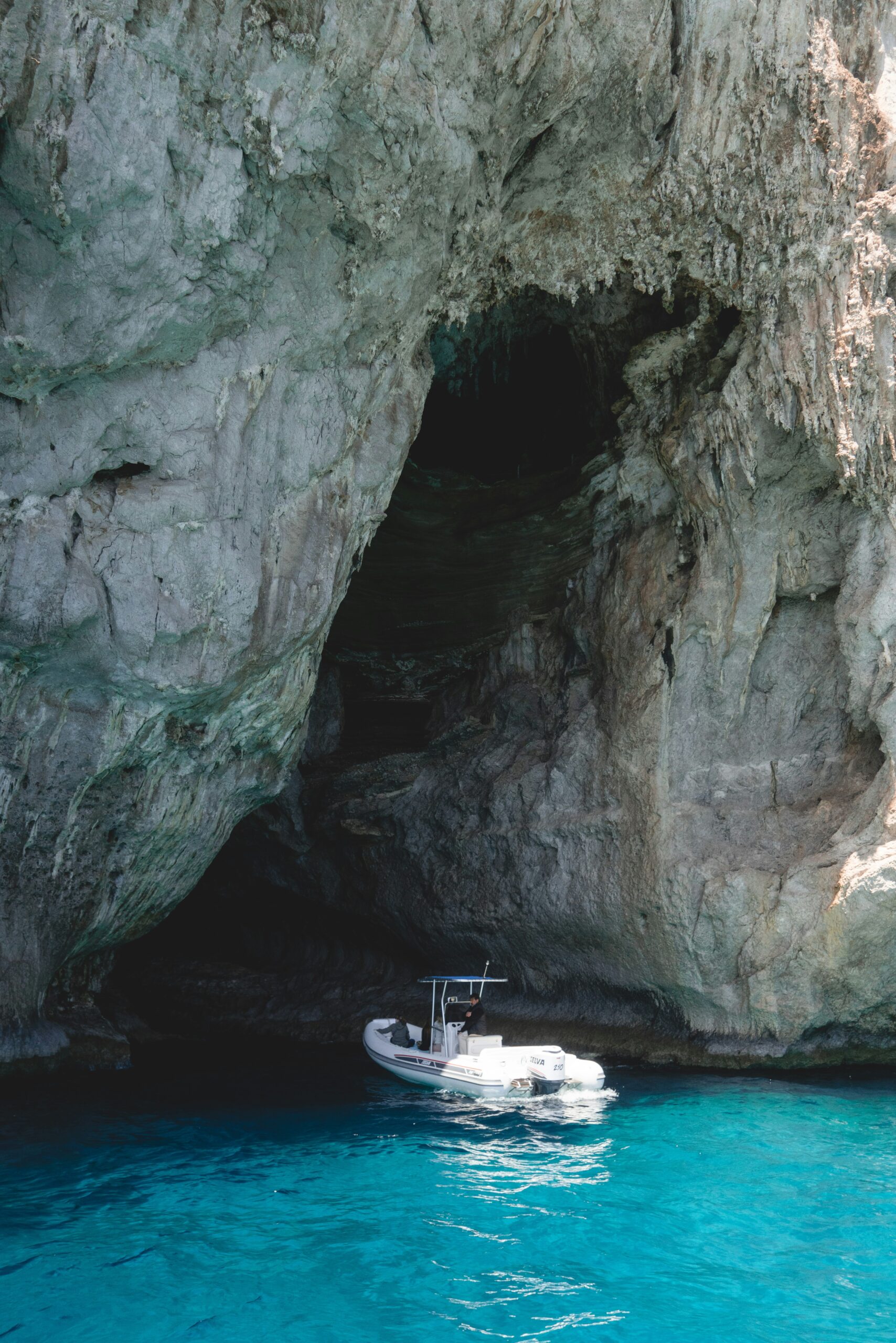 A small boat about to enter the Blue Grotto in Capri, Italy, captured just moments before passing through the narrow entrance. The turquoise waters shimmer under the sunlight, hinting at the magical luminescence within the grotto. The rugged cliffs frame the scene, emphasizing the natural beauty and allure of this famous attraction on Capri Island. This picturesque moment showcases the anticipation and excitement of exploring the stunning Blue Grotto, a must-visit destination for travelers to Capri, Italy.