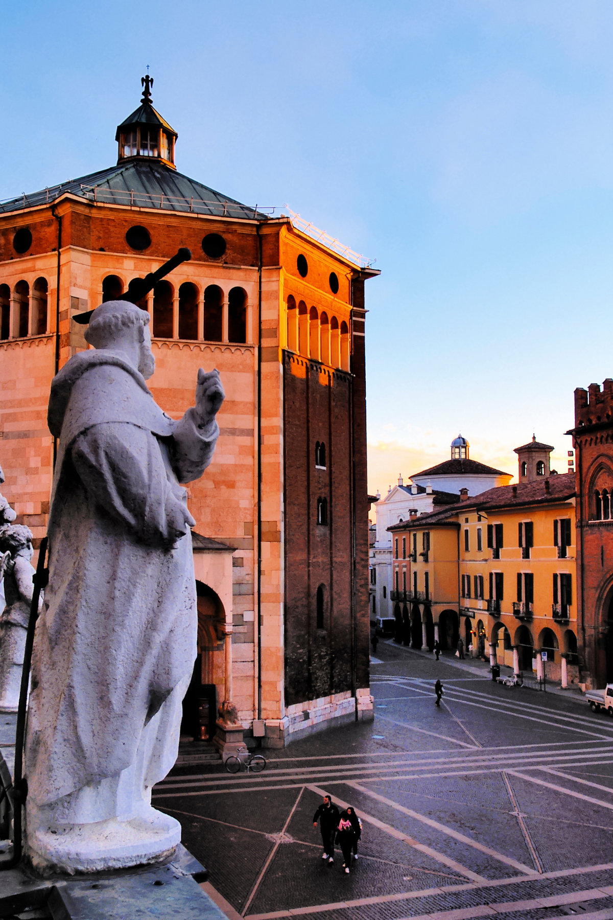 A detailed photograph features the magnificent Cremona Cathedral in Cremona, Italy, with its impressive Gothic and Romanesque architecture. In the foreground, a prominent statue adds a touch of historical significance, standing as a sentinel to the grand entrance. The cathedral's intricate facade, adorned with ornate carvings and sculptures, is bathed in soft sunlight, highlighting its architectural splendor. This image encapsulates the rich cultural heritage and artistic beauty of Cremona, Italy, making it a must-see landmark for travelers exploring this historic city.