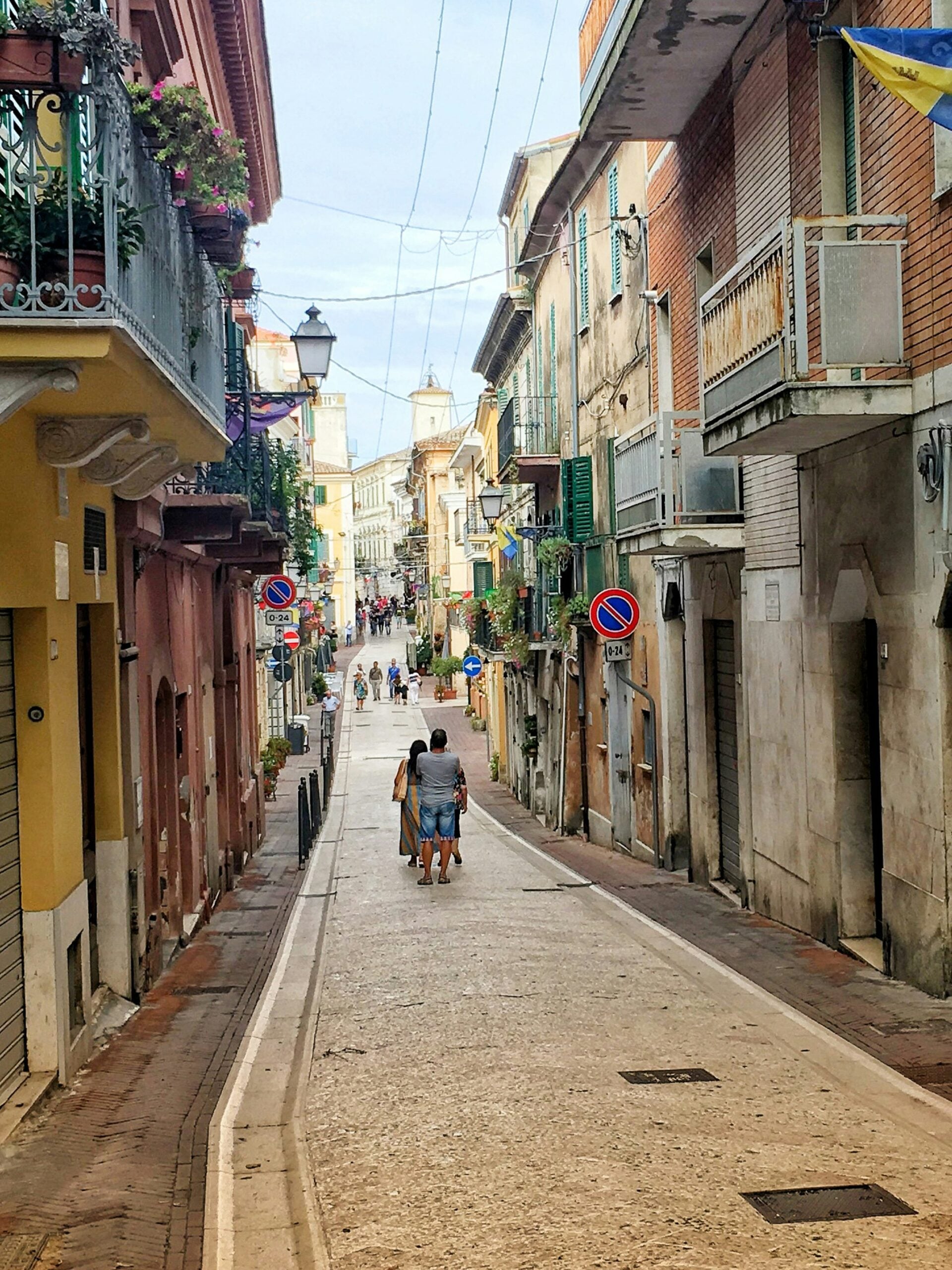 A charming road in Città Sant'Angelo, located in the Province of Pescara, Italy, with people leisurely walking along the cobblestone path. The scene captures the essence of this historic town, where narrow streets wind through picturesque buildings adorned with colorful shutters and flower boxes. Locals and visitors stroll along, enjoying the tranquil atmosphere and the scenic views that this elevated town offers. The road is lined with quaint shops, cafes, and traditional Italian architecture, creating a welcoming ambiance that invites exploration of Città Sant'Angelo's rich cultural heritage.