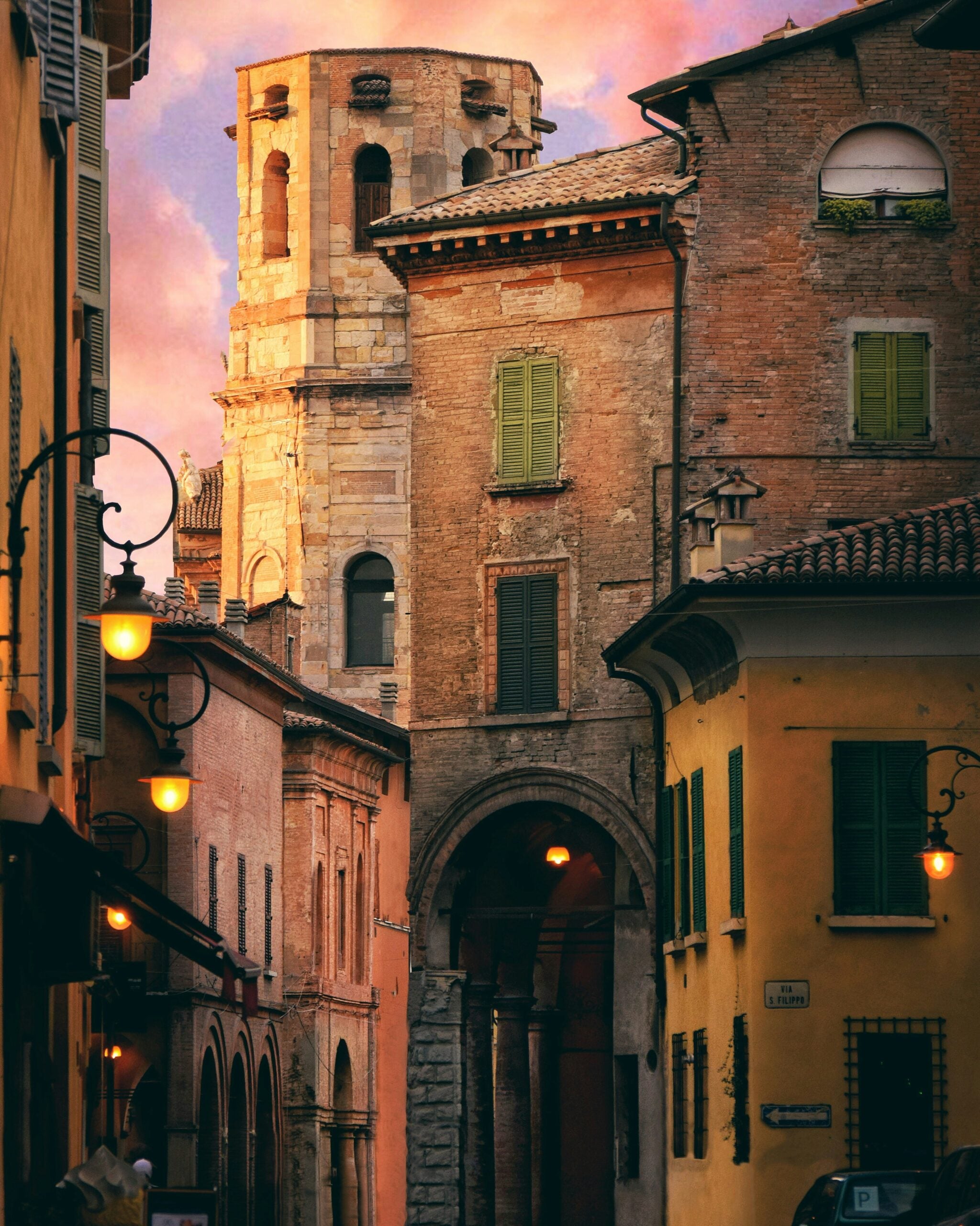 A photograph of Piazza Antonio Fontanesi in Reggio Emilia, Italy, captures the lively atmosphere of this charming square. The image showcases the piazza's expansive open space, surrounded by historic buildings with classic Italian architecture, featuring arched windows and elegant facades. The square is lined with trees that provide shade, while outdoor cafés and restaurants with tables and chairs invite visitors to relax and enjoy the vibrant ambiance. Locals and tourists alike are seen strolling or sitting, soaking in the tranquil yet lively environment. This picturesque scene encapsulates the social and cultural heart of Reggio Emilia, Italy, making it a must-visit spot in the city.