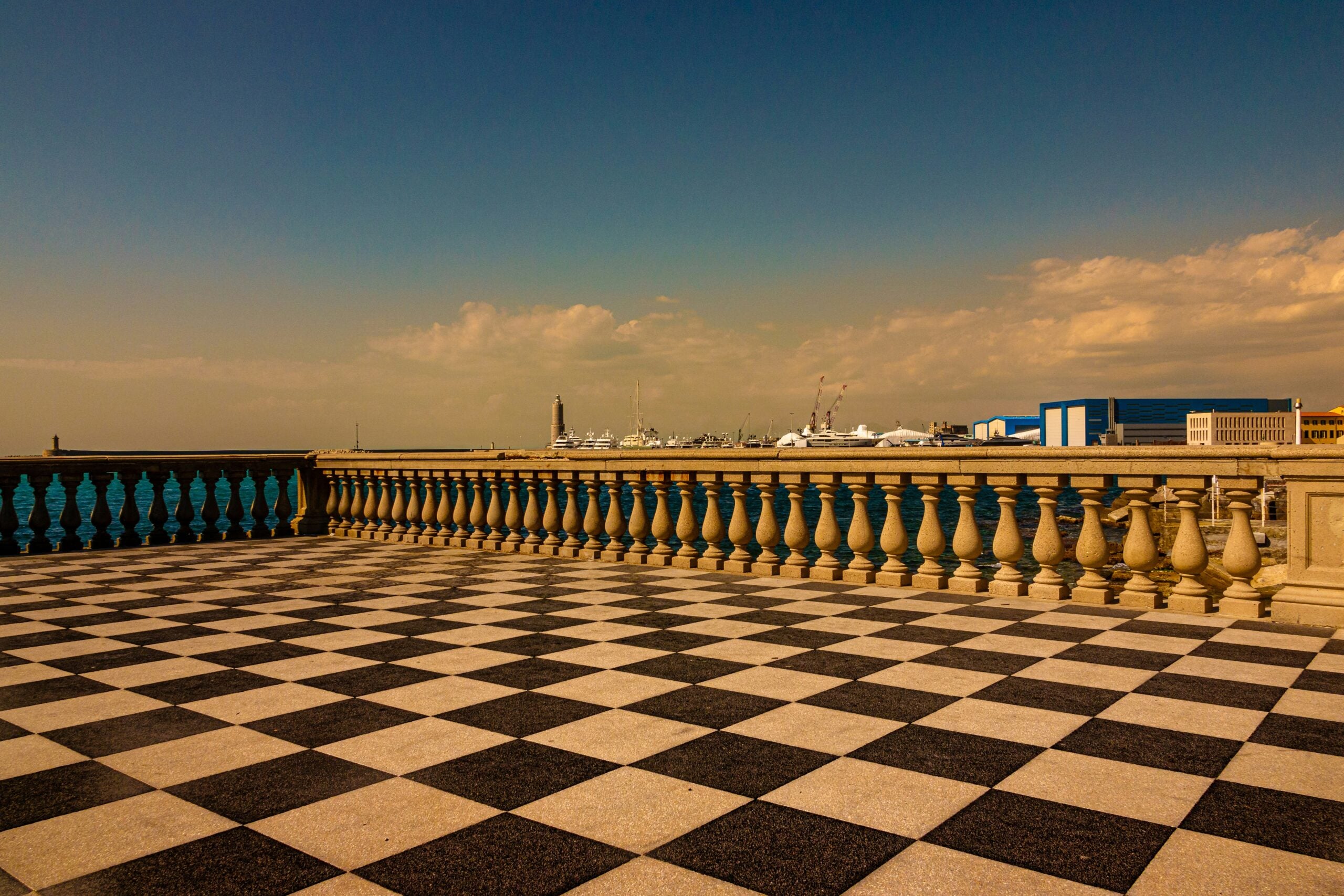 A stunning view of Piazza Mascagni in Livorno, located in the Province of Livorno, Italy, showcases the iconic checkered black and white promenade that stretches out towards the sea. The geometric pattern of the terrace creates a visually striking foreground, with the calm waters of the Mediterranean Sea and the sky blending into soft hues at the horizon. The elegant balustrades and nearby historic buildings add to the charm of this popular gathering spot. This image captures the essence of Livorno's coastal beauty, making Piazza Mascagni a must-see landmark in the city.