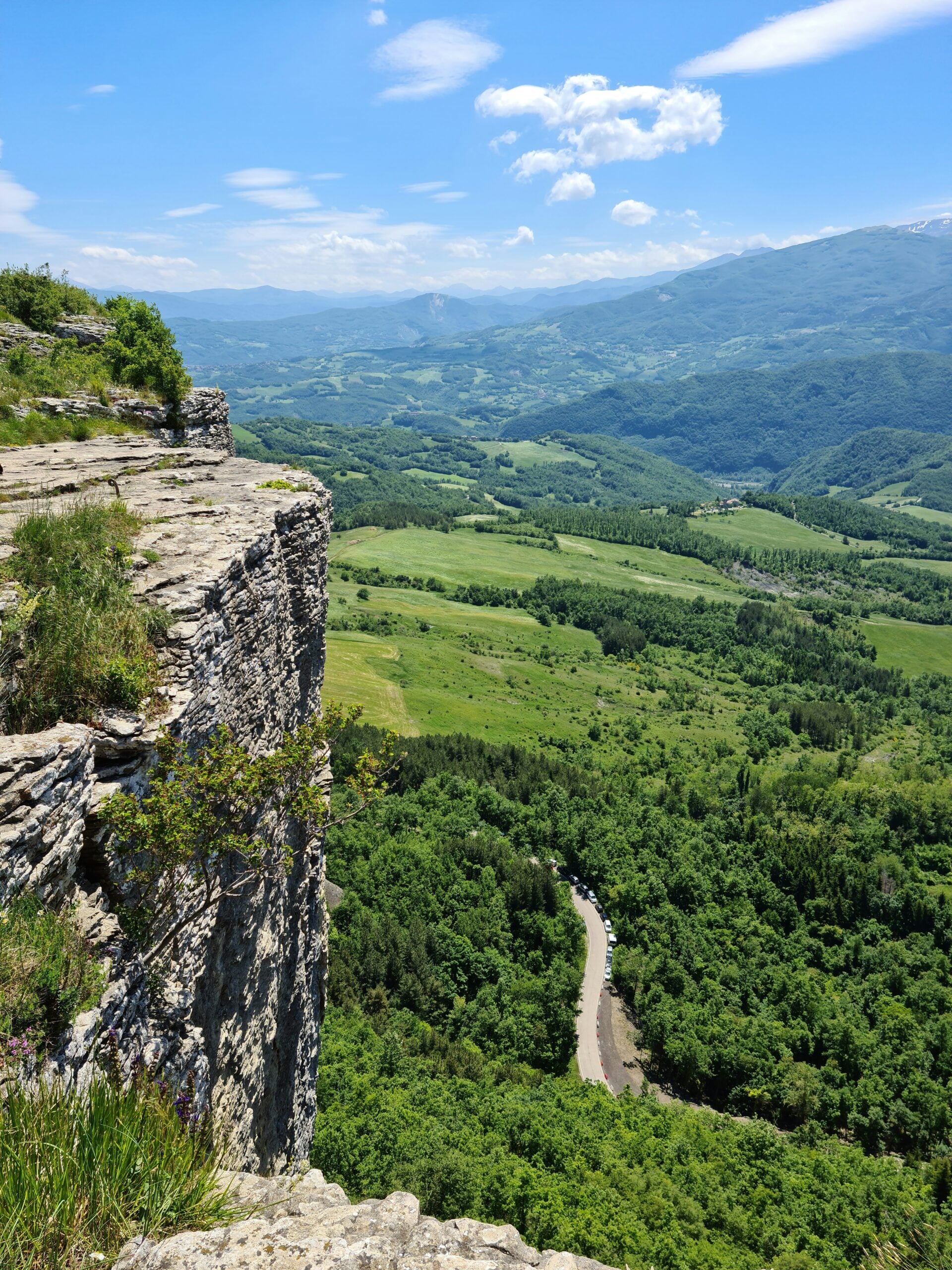 A photograph of Pietra di Bismantova in Castelnovo ne' Monti, Reggio Emilia, Italy, captures the striking natural beauty of this iconic geological formation. The towering rock plateau rises dramatically from the surrounding landscape, with sheer cliffs and rugged edges that dominate the view. The base of the formation is surrounded by lush green forests and rolling hills, creating a stunning contrast with the rocky terrain. The sky above is clear, highlighting the majestic presence of Pietra di Bismantova. This scene showcases the breathtaking natural wonders of Reggio Emilia, Italy, making it a popular destination for hikers, nature lovers, and those seeking to experience the region's unique landscape.