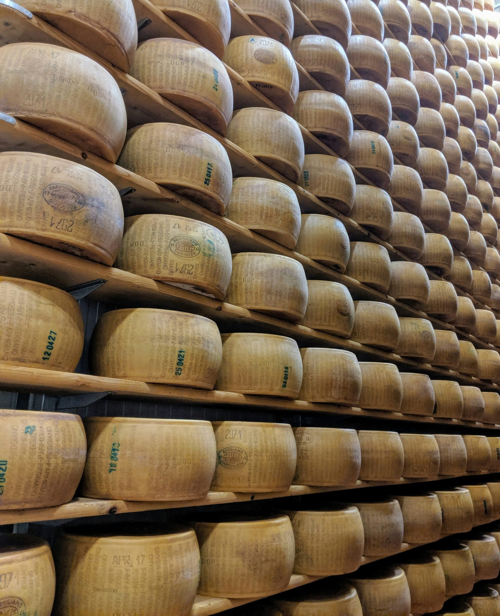 A photograph taken in Reggio Emilia, Province of Reggio Emilia, Italy, features impressive stacks of cheeses, showcasing the region's renowned culinary heritage. The image highlights rows of large, wheel-shaped Parmigiano-Reggiano cheeses, carefully aged and stacked in a traditional storage area. The golden hues of the cheese wheels contrast beautifully with the rustic wooden shelves, emphasizing the craftsmanship and tradition behind this iconic Italian product. This scene captures the essence of Reggio Emilia's rich gastronomic culture, where cheese-making is both an art and a time-honored tradition, celebrated worldwide.