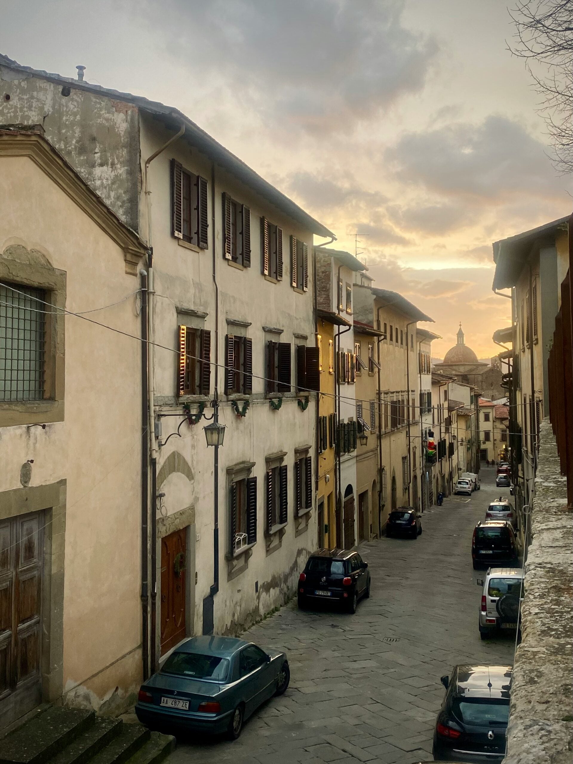 The image offers a breathtaking view from Giorgio Vasari's house in Arezzo, Tuscany. From this vantage point, the rolling hills of the Tuscan countryside stretch into the distance, bathed in warm sunlight. The rooftops of Arezzo's historic buildings, with their terracotta tiles and stone facades, spread out below, leading the eye toward the city's prominent medieval towers and church spires. The scene captures the tranquil beauty of Tuscany, blending the rich architectural heritage of Arezzo with the serene natural landscape. This view is a perfect representation of the timeless charm and cultural richness found in Arezzo, Tuscany.