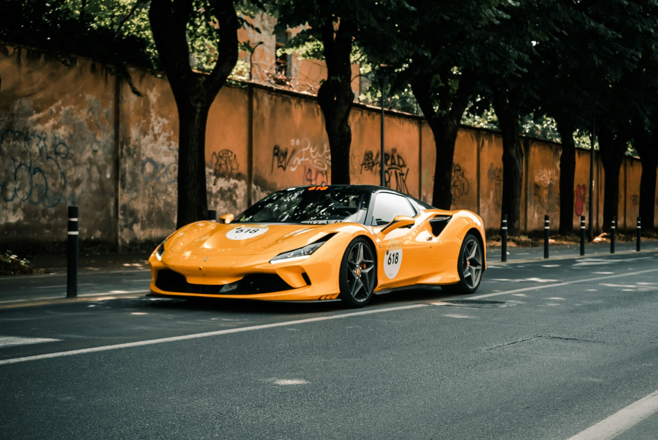 Dynamic photograph of a yellow Ferrari cruising along an urban street in Brescia, Italy, with colorful graffiti adorning the walls. This image captures the fusion of contemporary luxury and vibrant street art, showcasing Brescia's unique urban charm and cultural flair. Ideal for those interested in the lively, artistic side of Italian cities.