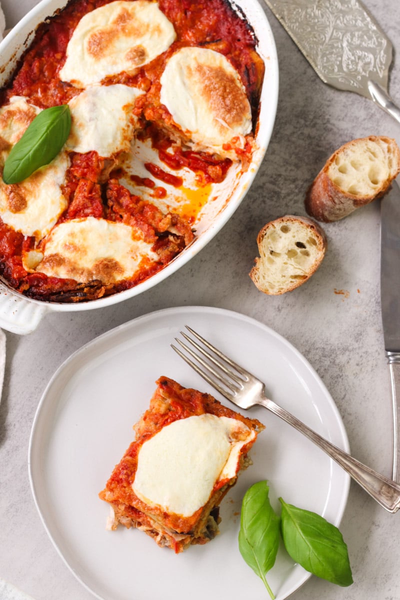 overhead image of parmigiana di Melanzane (Traditional Eggplant Parmigiana) in a white casserole and on a white plate.