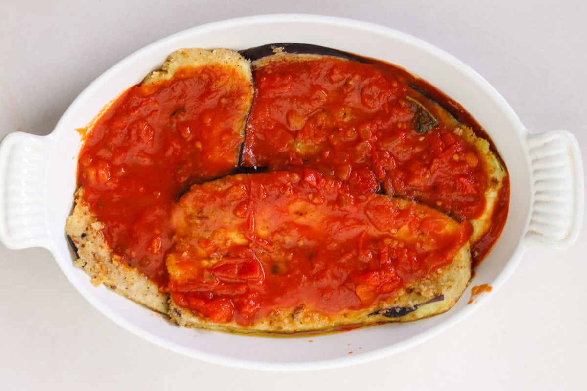 overhead image of layering eggplant in white casserole for Parmigiana di Melanzane (Traditional Eggplant Parmigiana)