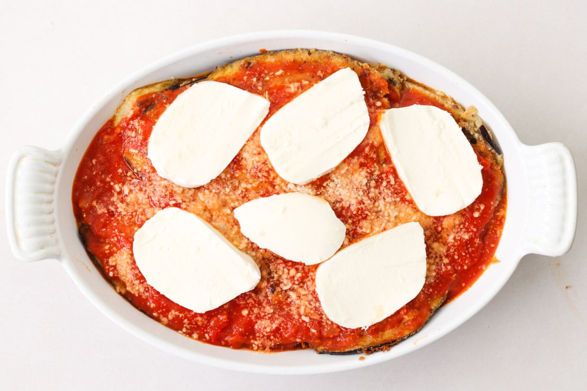 overhead image of making eggplant parmesan in a white casserole.