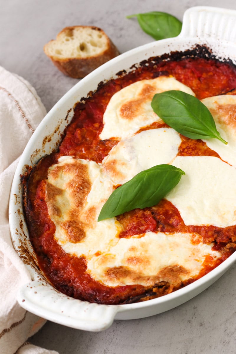 close up image of Parmigiana di Melanzane (Traditional Eggplant Parmigiana)in a white baking dish.