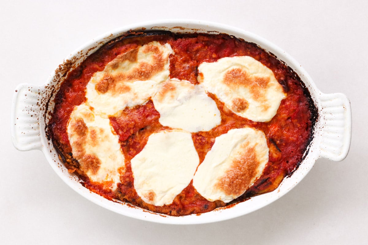 overhead image of making Parmigiana di Melanzane (Traditional Eggplant Parmigiana)in white casserole.