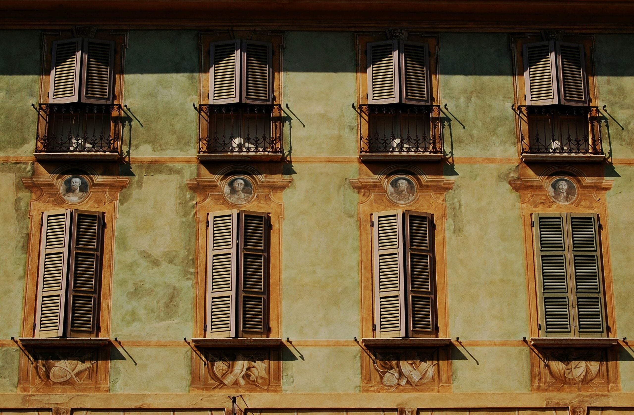 Photograph of a palace facade in Brescia, featuring elegant windows with shutters and sunshades. This image captures the architectural detail and charm of the building, highlighting the practical yet stylish design elements that provide shade and privacy. The sunshades add a functional elegance, enhancing the historical ambiance of Brescia's urban landscape.