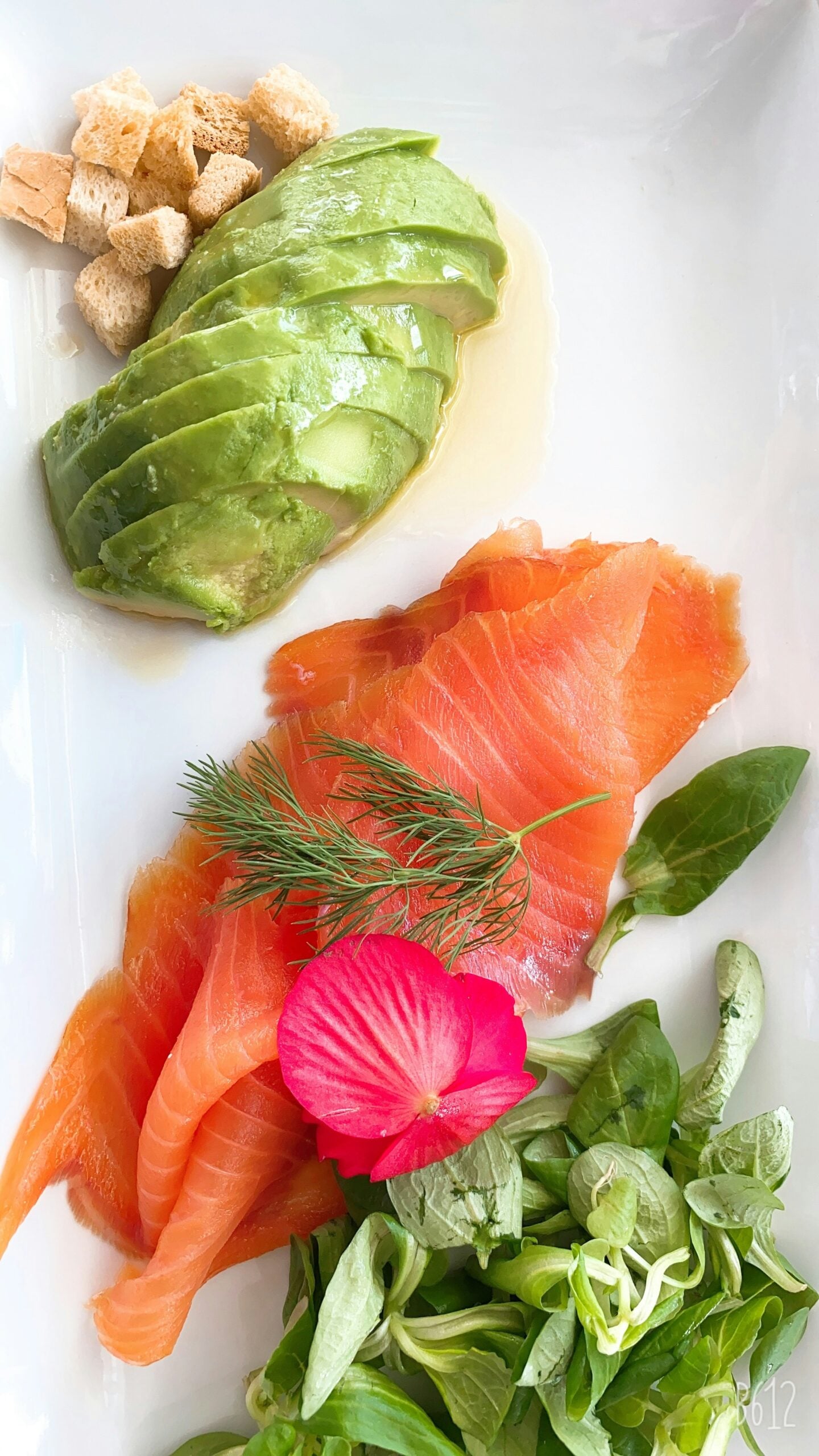 A fresh and appetizing lunch scene at a mall in Sanremo, Italy, featuring a beautifully plated dish of smoked salmon with avocado. The vibrant orange-pink slices of smoked salmon are artfully arranged alongside creamy, green avocado slices, garnished with a sprinkle of herbs and a drizzle of olive oil. The dish is served on a sleek white plate, enhancing the contrast of colors and emphasizing the freshness of the ingredients. The setting, within the casual yet stylish atmosphere of the mall, adds to the modern dining experience in Sanremo, offering a taste of both local flavors and international cuisine.