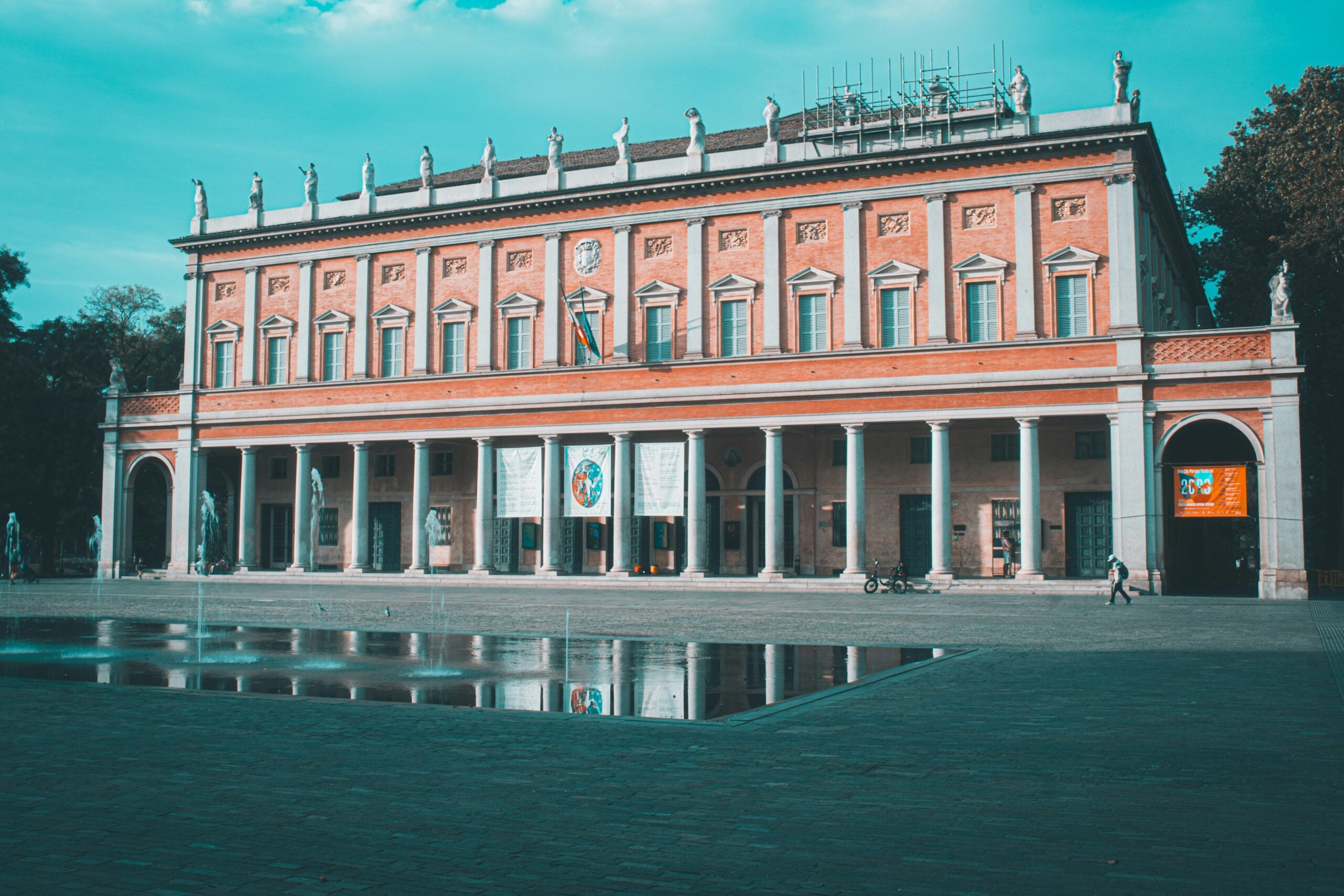 A photograph of a municipal building in Reggio Emilia, Italy, showcases the elegant architecture that reflects the city's rich history and civic pride. The building's facade features classic Italian design elements, such as arched windows, ornate balconies, and a grand entrance framed by decorative columns. The well-maintained exterior, set against the backdrop of a bustling city square, highlights the importance of this government structure within the community. This image captures the essence of Reggio Emilia, Italy, blending tradition with the city's vibrant public life.