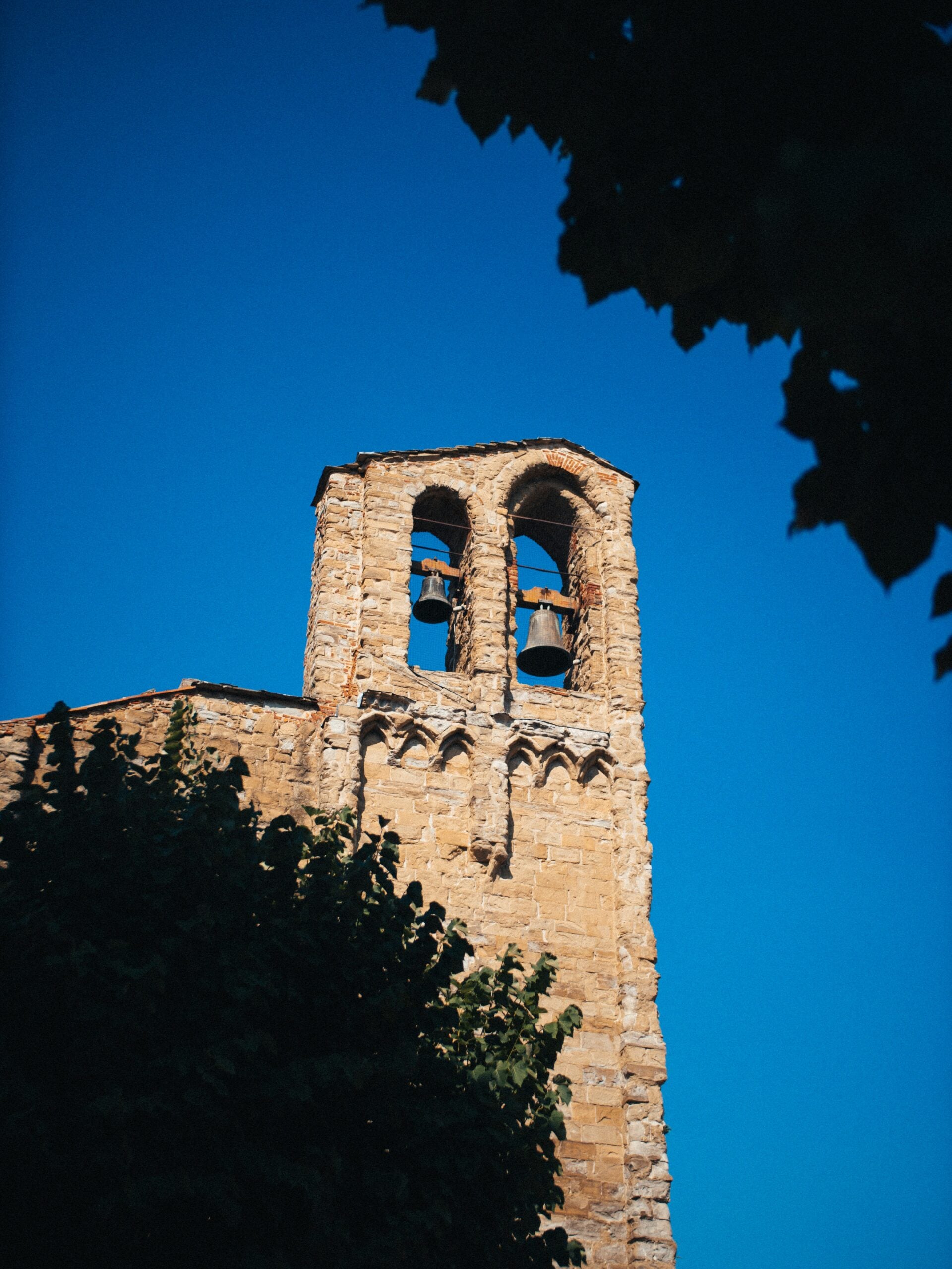 The image shows an old tower in Arezzo, Italy, characterized by its rustic stone structure and historical charm. The tower prominently features two large church bells, which are visible through arched openings near the top. This architectural gem stands as a testament to Arezzo’s rich heritage, with the weathered stone and traditional design reflecting the town’s medieval past. The tower is a striking feature against the backdrop of Arezzo's picturesque skyline, making it a significant landmark for visitors interested in exploring the historical and cultural treasures of this beautiful Italian city.