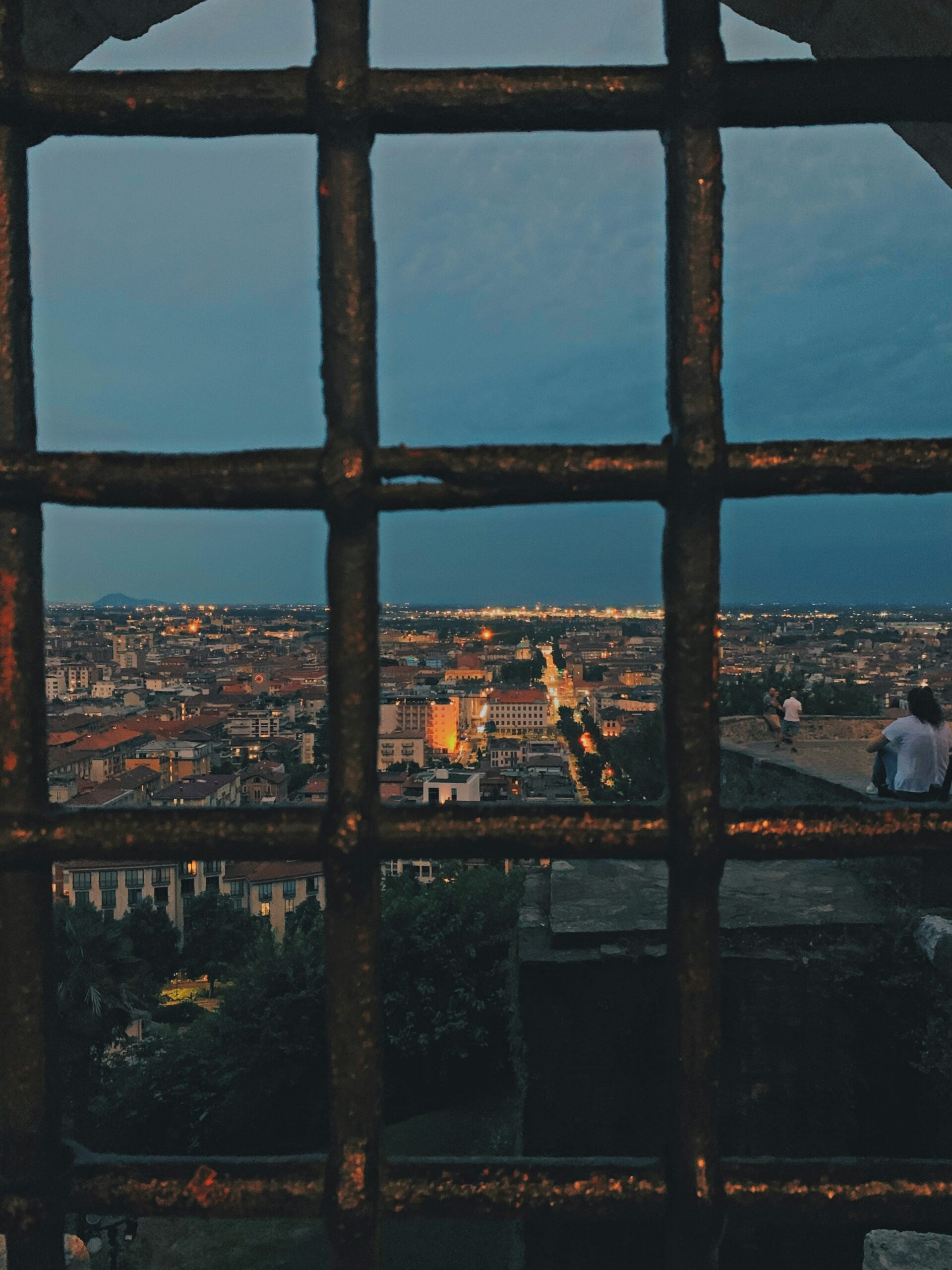A stunning panoramic view of Bergamo, Italy, at night, taken from Vicolo Salita della Scaletta 3. The photograph captures the city's enchanting nighttime ambiance, with the lights of the Città Bassa and Città Alta twinkling below. The historic buildings and medieval towers are illuminated, creating a captivating contrast against the dark sky. The winding streets and distant hills are subtly outlined, adding depth to the scene. This breathtaking view showcases the romantic and timeless allure of Bergamo, Italy, offering a glimpse into the city's vibrant life after sunset.