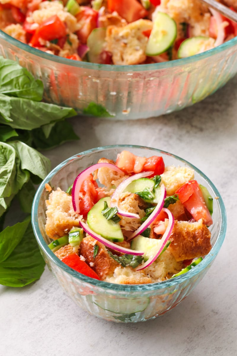 closeup image of panzanella salad in glass bowls and basil on the side.
