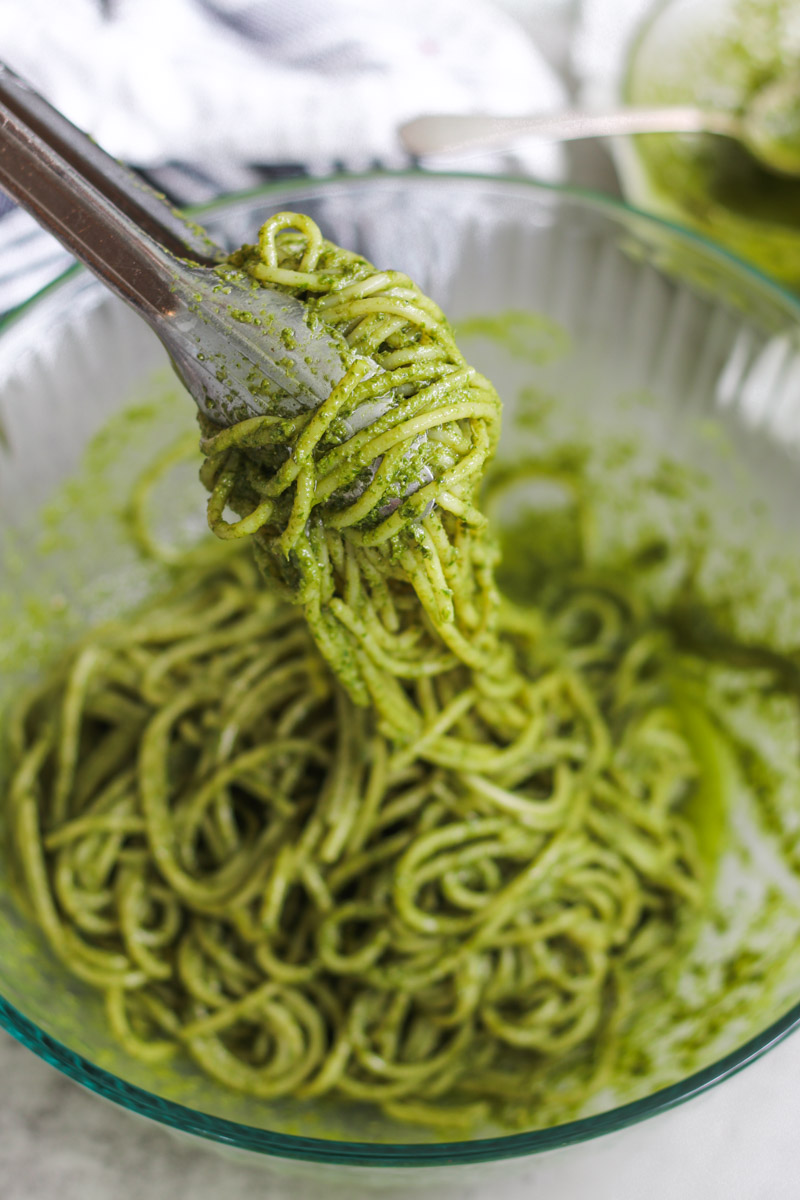 close up image of spaghetti wtih pesto sauce in a glass bowl.