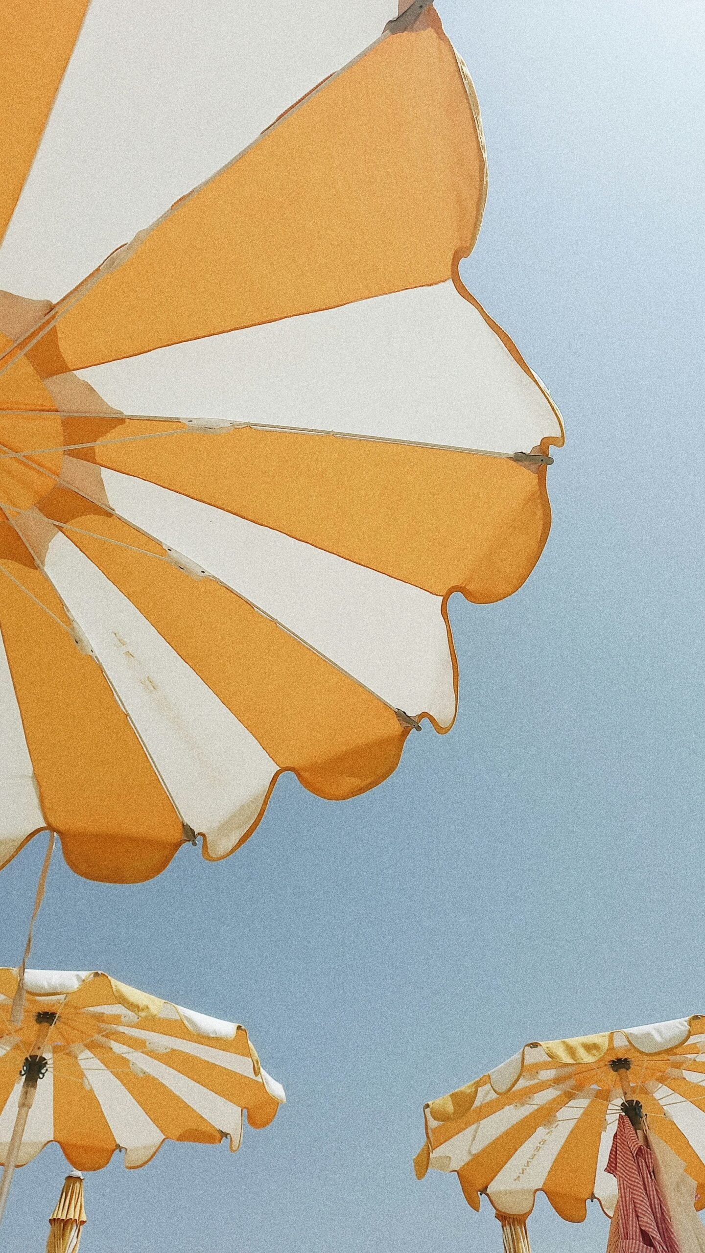 A bright and cheerful summer scene in Sanremo, Italy, featuring a row of yellow and white striped umbrellas set against a brilliant blue sky. The umbrellas, positioned along the sandy beach, create a vibrant and inviting atmosphere, perfect for a day of relaxation by the Mediterranean Sea. The contrasting colors of the yellow and white umbrellas against the deep blue sky emphasize the sunny, warm weather typical of summer in Sanremo. This image encapsulates the joyful and leisurely spirit of a summer day in this beautiful Italian coastal town, where the seaside and the sun play a central role in the local lifestyle.