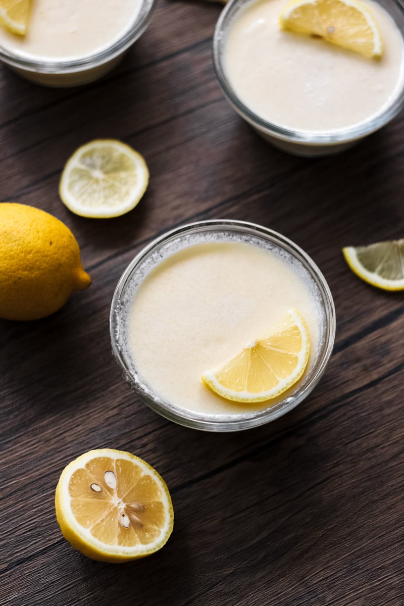 close up image of crema al limone in glass bowls and lemons in the background.