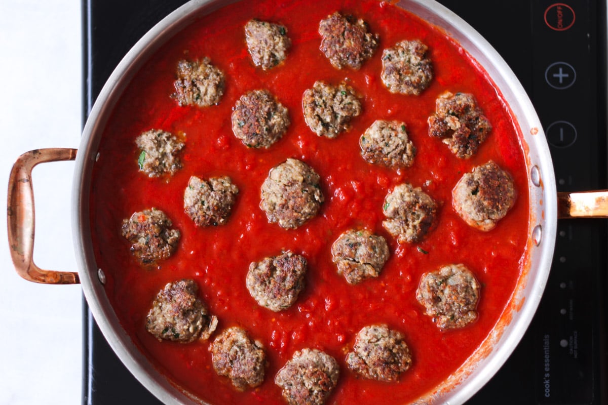 close up image of meatballs cooking in tomato sauce.